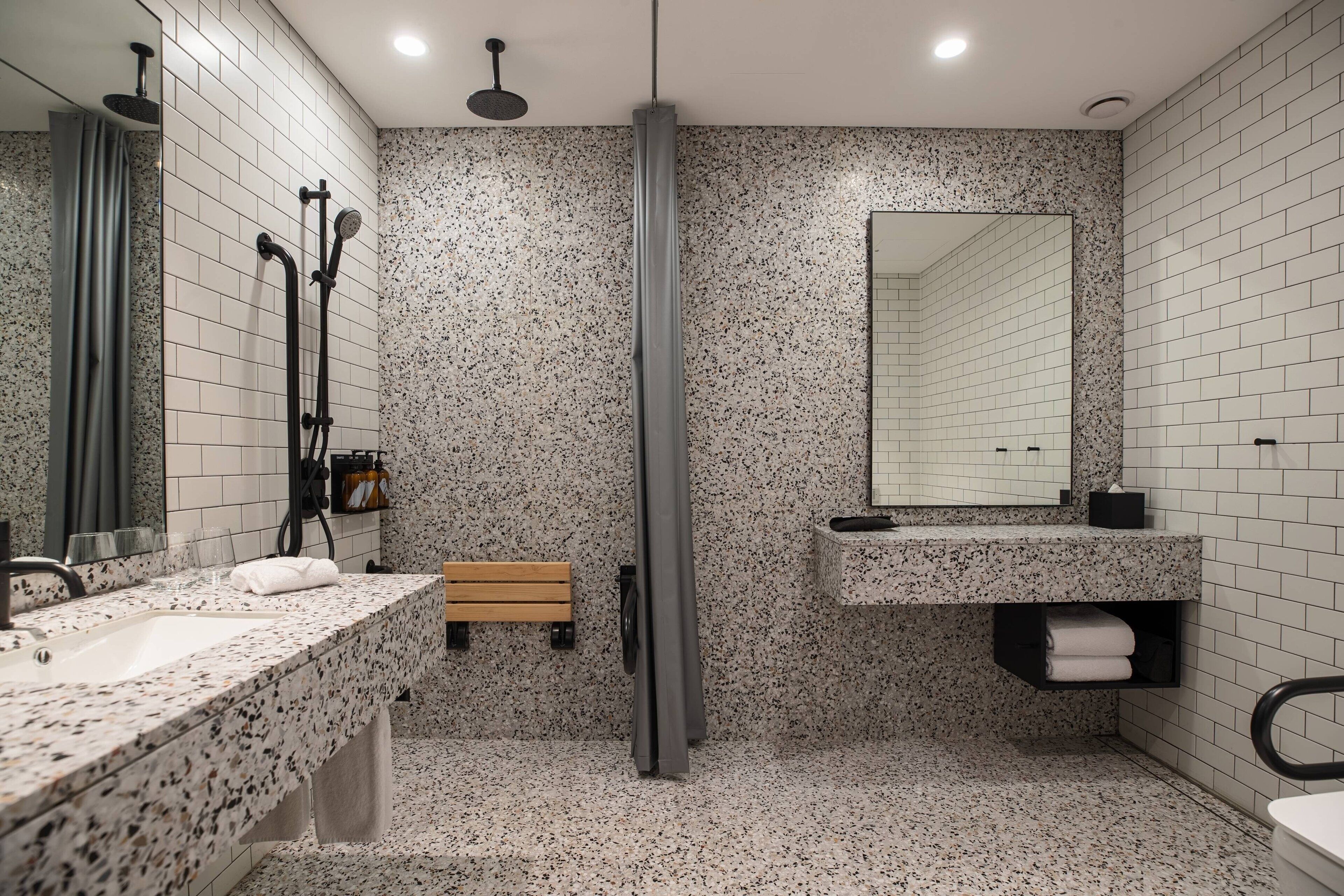 A modern bathroom with a granite countertop sink, a mirror, a shower enclosure, and a bench.