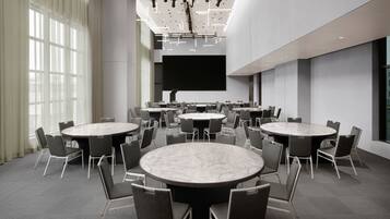 A modern conference room with multiple round tables and chairs, a large screen, and a ceiling with track lighting.