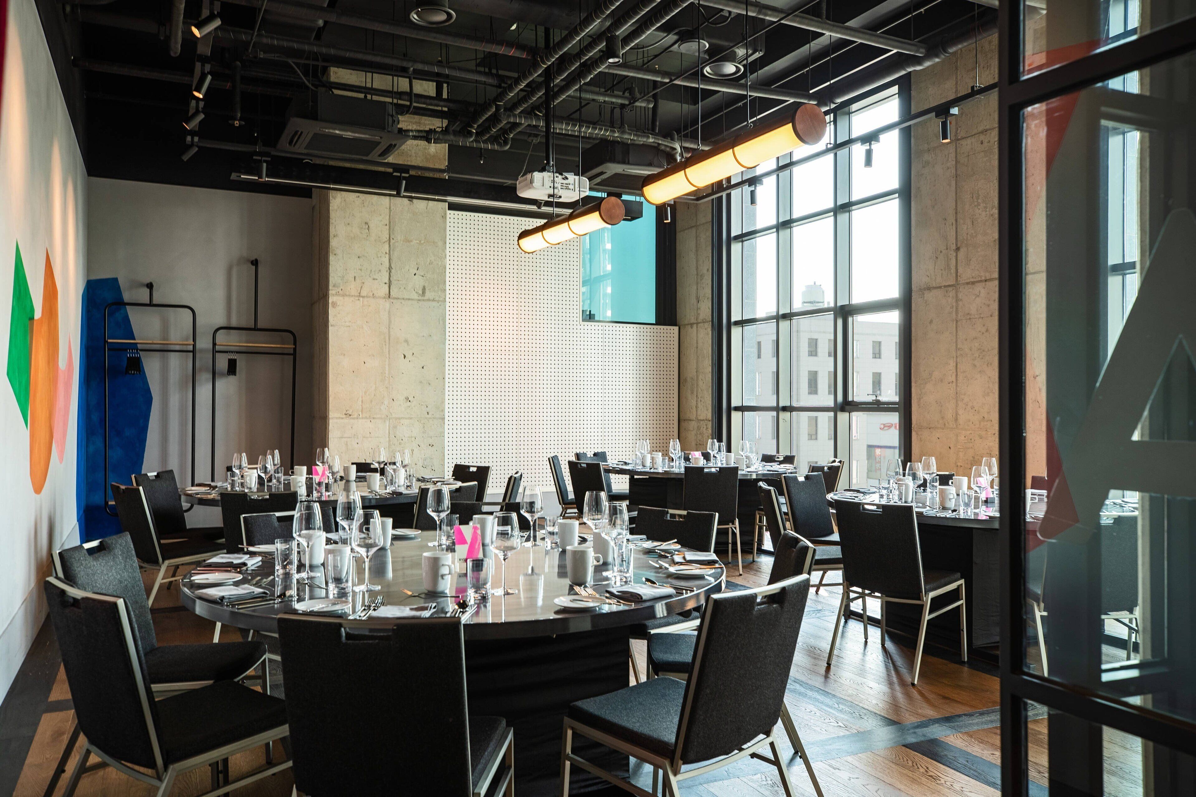 A conference room with round tables, black chairs, and glassware.