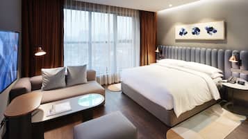A modern hotel room with a large bed, a sofa, a coffee table, and a TV.