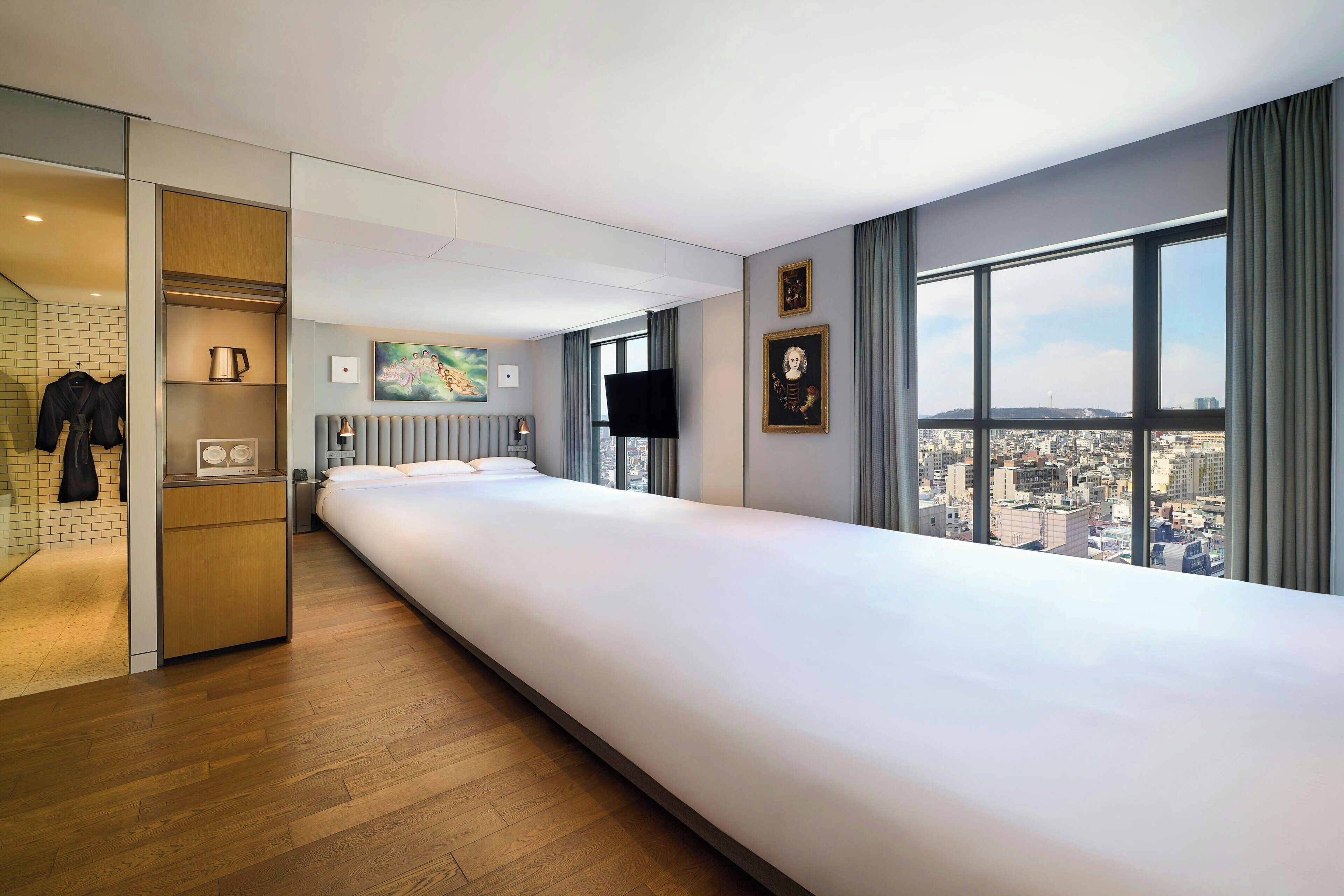 Ein modernes Hotelzimmer mit einem großen Bett, Blick auf die Stadt, einem Flachbildfernseher und einer kleinen Küchenzeile.