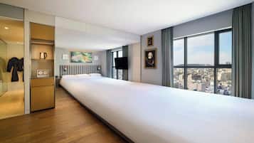 Ein modernes Hotelzimmer mit einem großen Bett, Blick auf die Stadt, einem Flachbildfernseher und einer kleinen Küchenzeile.