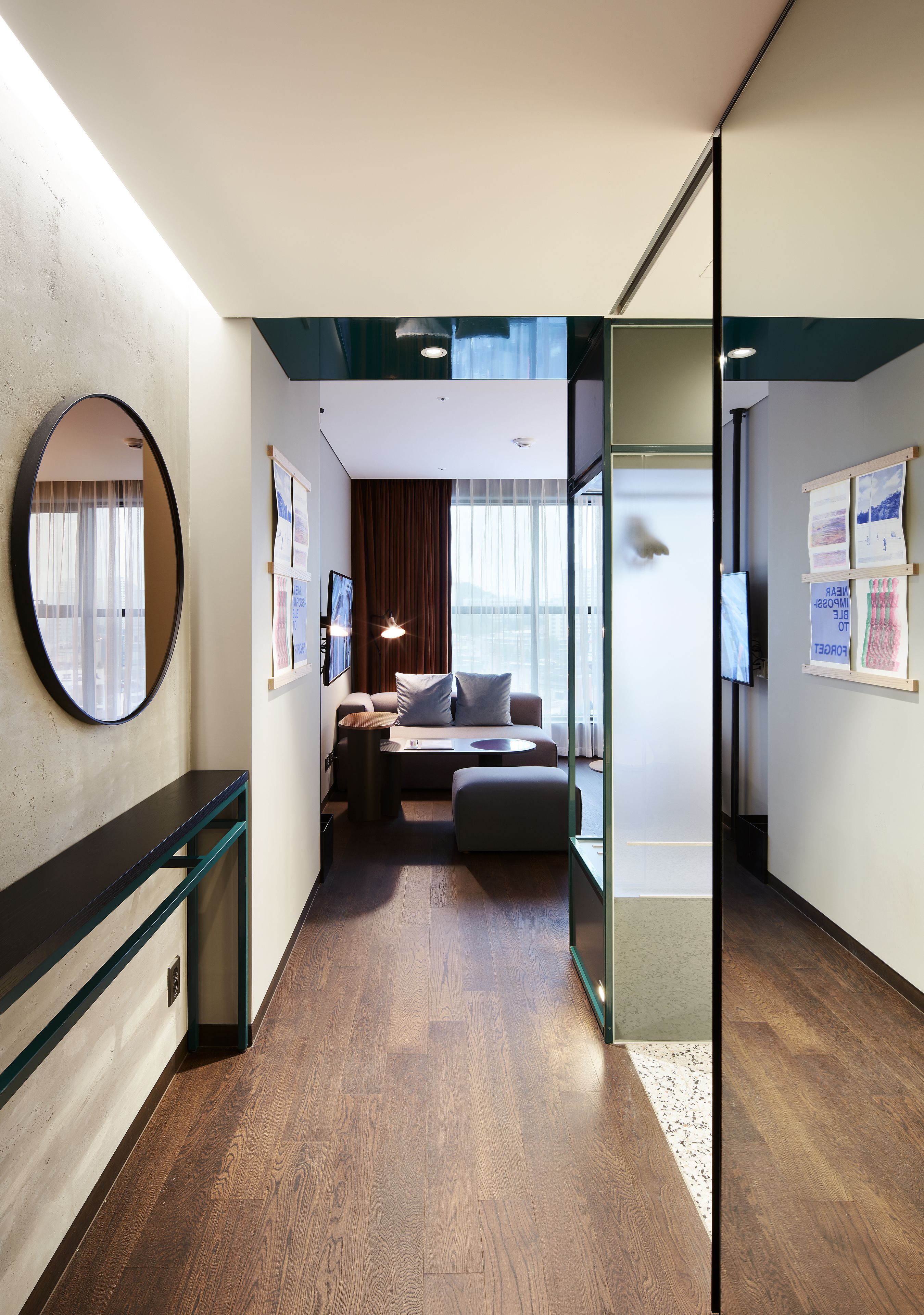 A modern hotel room with a wooden floor, a round mirror, a bed with a view, a small table, and a sofa.