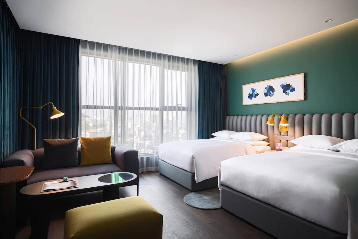 A hotel room with two beds, a sofa, a coffee table, and a desk.