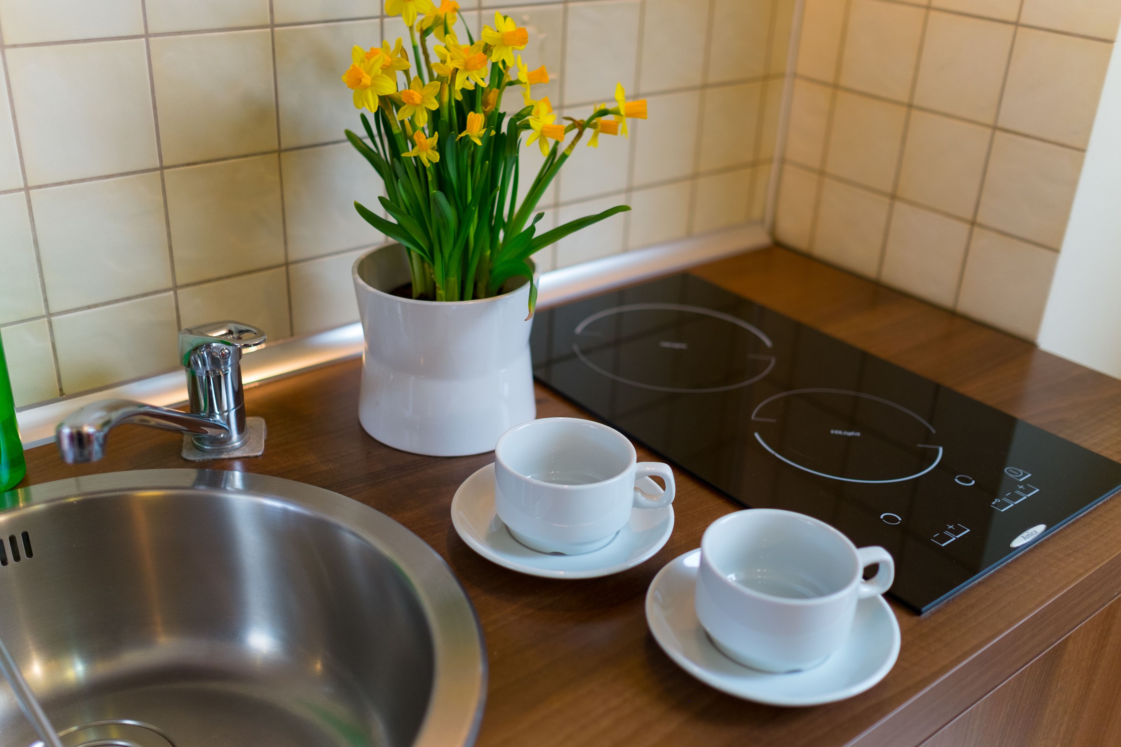 A kitchen with a stainless steel sink, a white electric stove, and a white cup on a saucer.