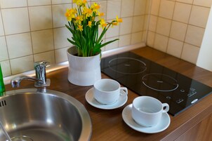 Una cocina con un lavamanos de acero inoxidable, una estufa eléctrica blanca y una taza blanca sobre un platillo.