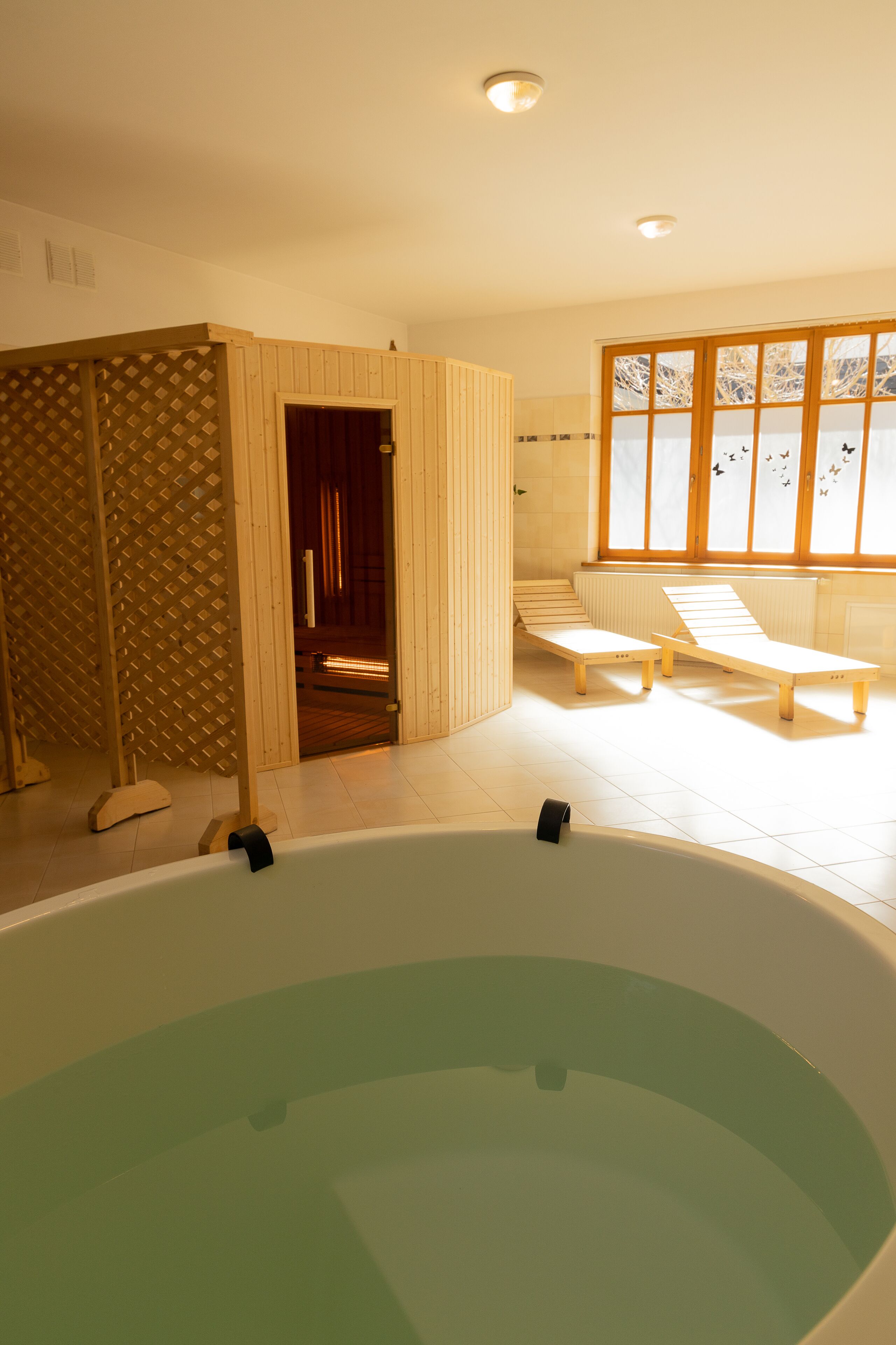 Un cuarto de spa con una bañera grande, bancos de madera y una puerta corrediza que da a una zona de sauna.