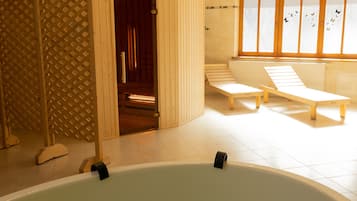 Un cuarto de spa con una bañera grande, bancos de madera y una puerta corrediza que da a una zona de sauna.