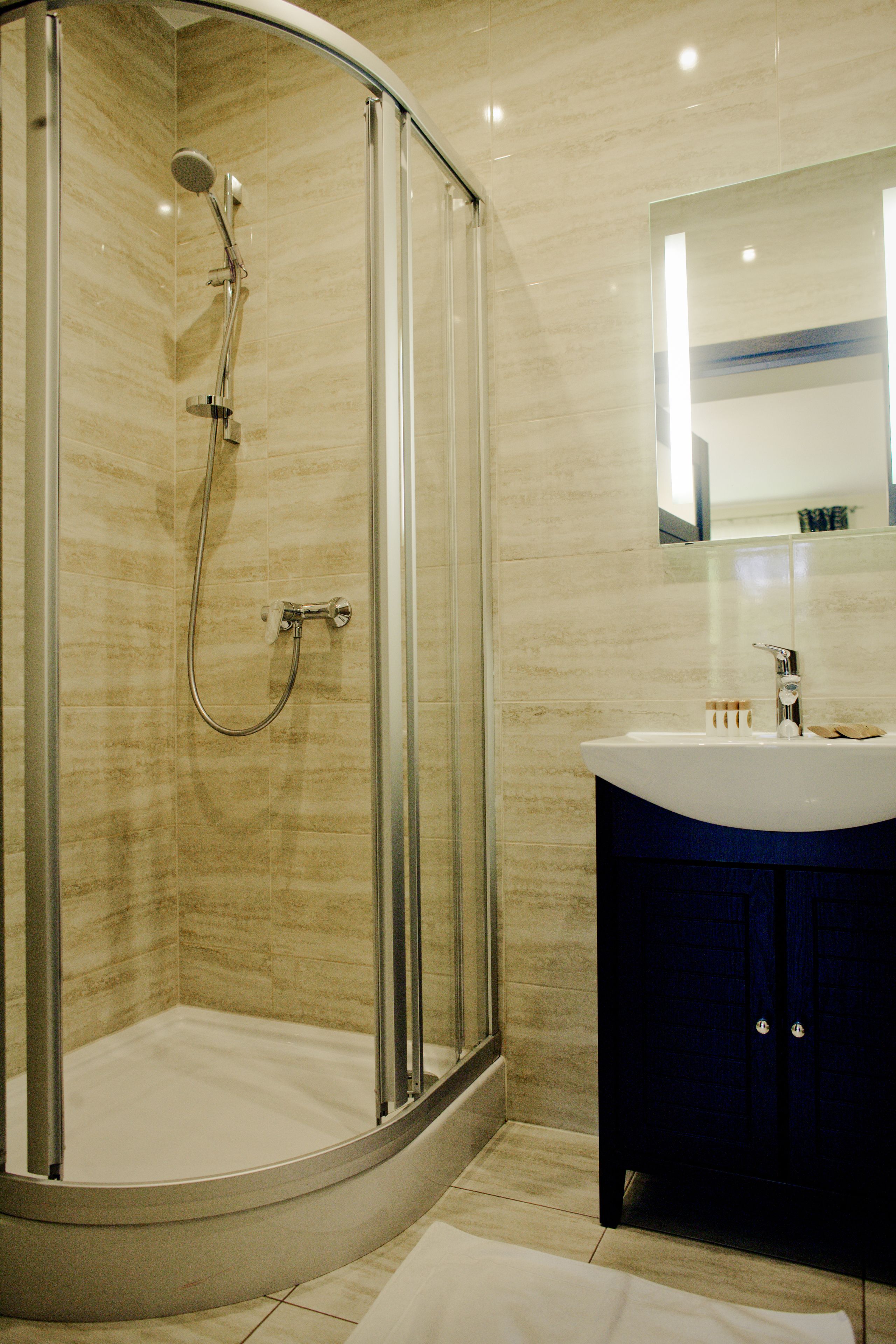 Un baño moderno con ducha envuelta en vidrio, un lavamanos blanco y un mueble de color oscuro.