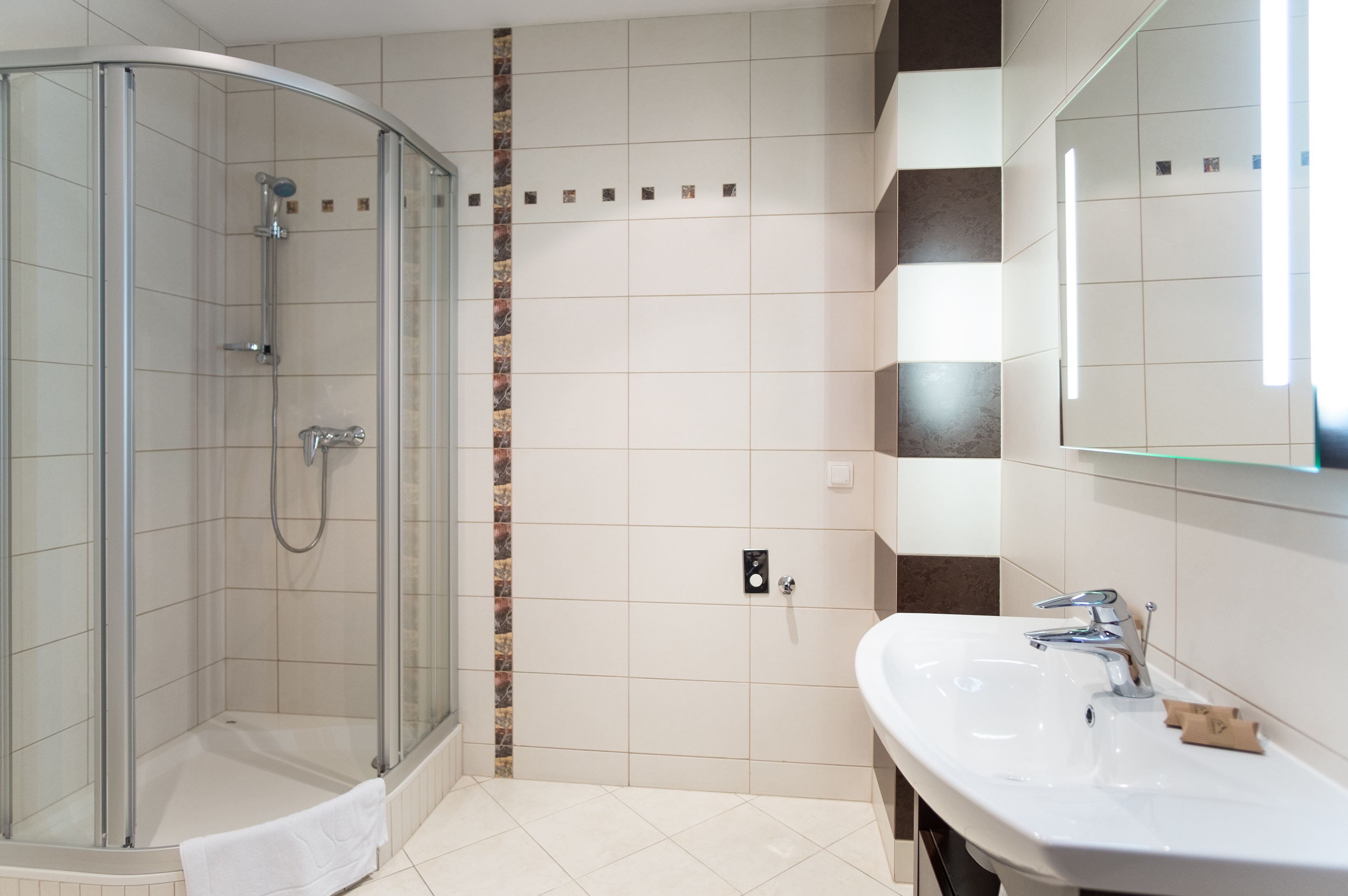 A modern bathroom with a glass-enclosed shower, a white sink with a mirror, and tiled walls.