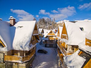A snow-covered lodge with wooden architecture, a car parked in front, and a clear blue sky.