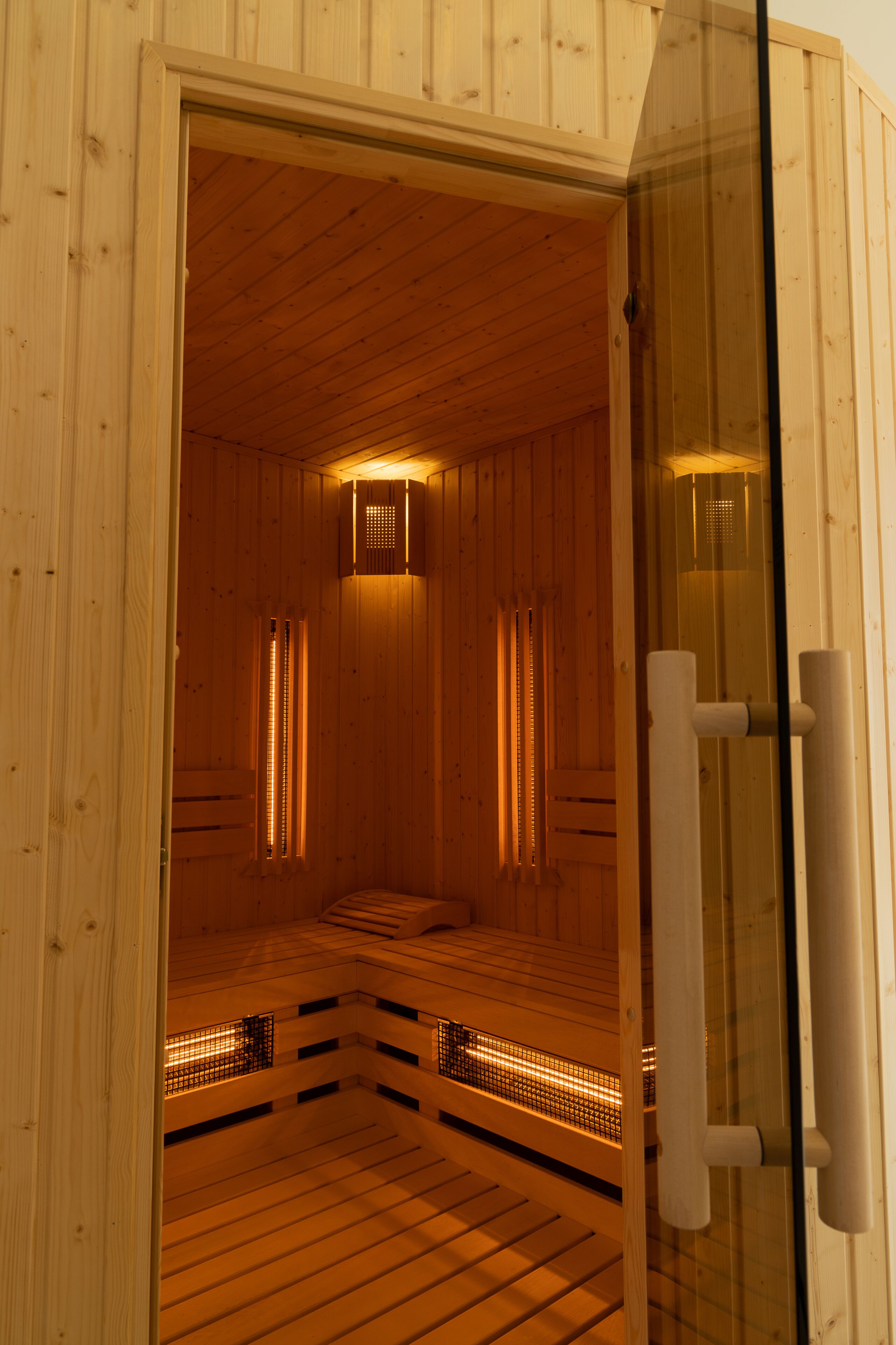 A sauna with wooden walls and a glass door, featuring a bench and a bench with a mesh backrest.