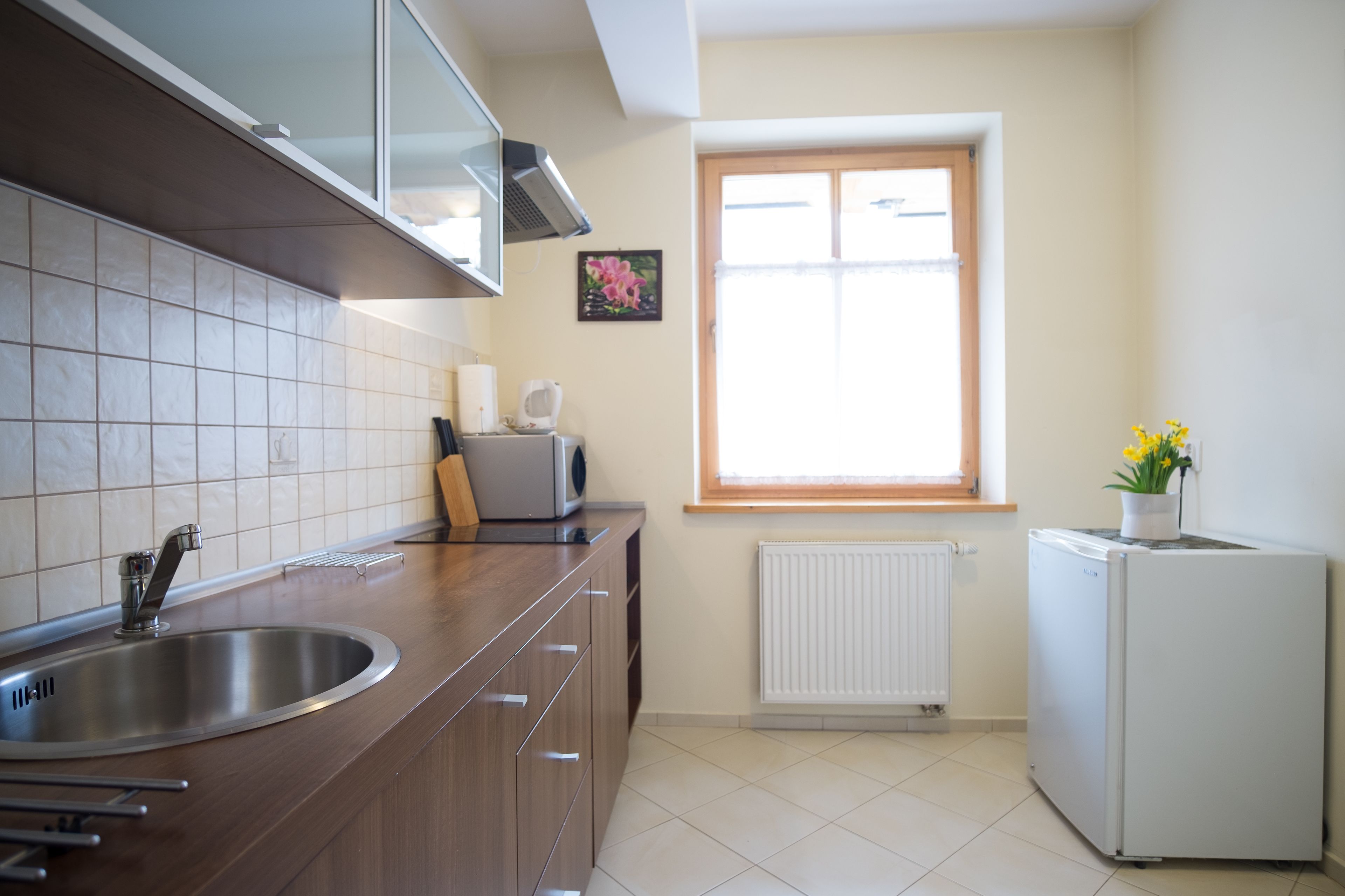 A kitchen with a stainless steel sink, wooden cabinets, a white refrigerator, and a window with a view of the outdoors.