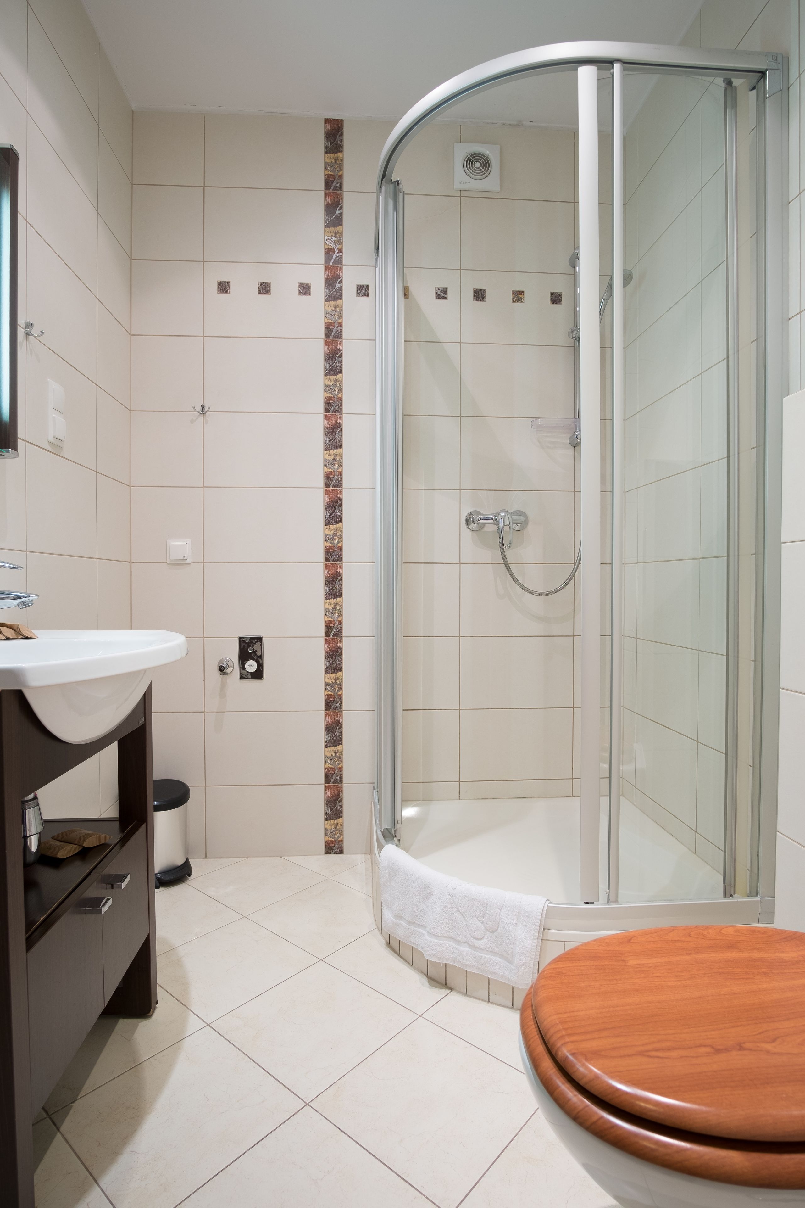Un baño con ducha envuelta en vidrio, inodoro de madera y lavamanos blanco con espejo arriba.