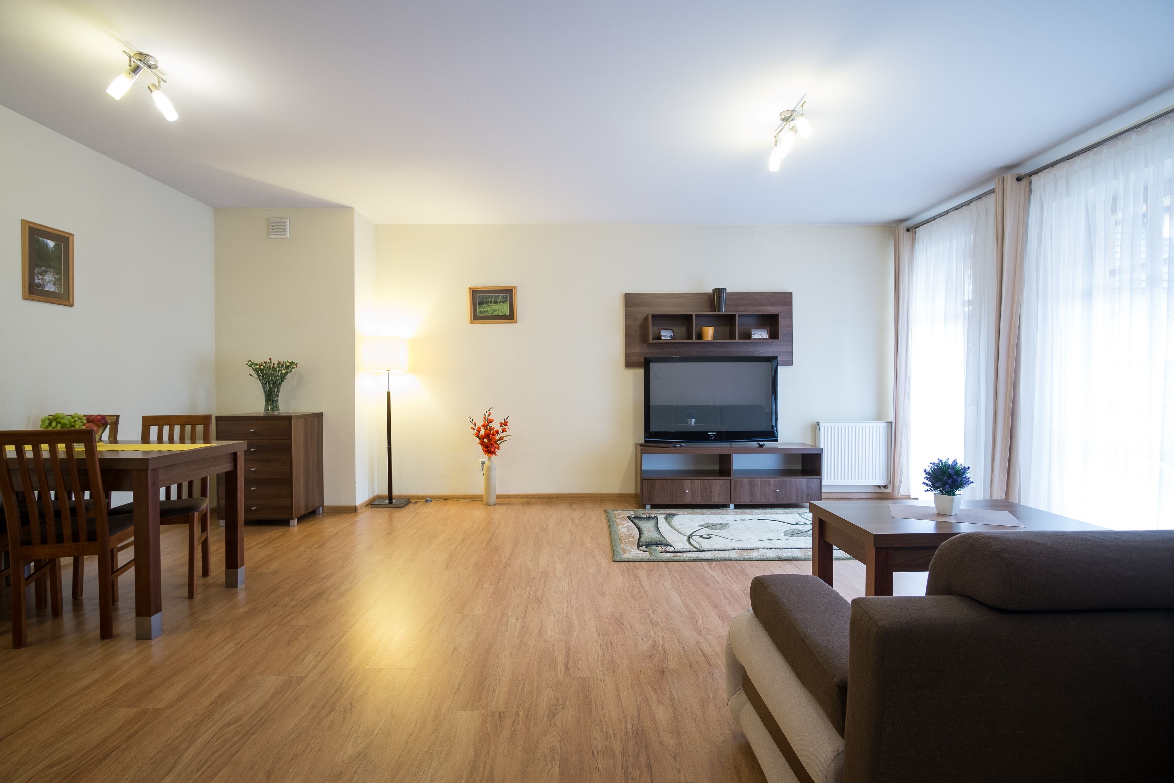A living room with a flat-screen TV, wooden furniture, and a large window with curtains.