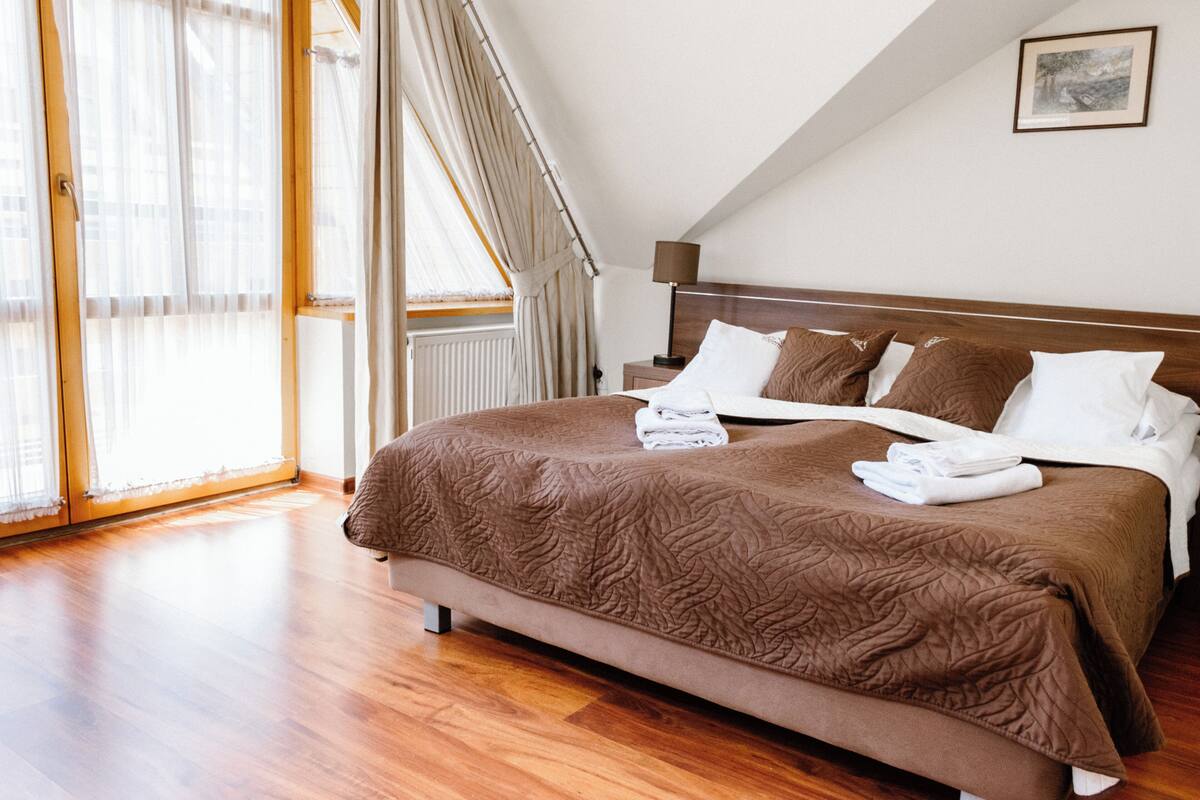 A bedroom with a large bed, a wooden headboard, a window with curtains, and a radiator.