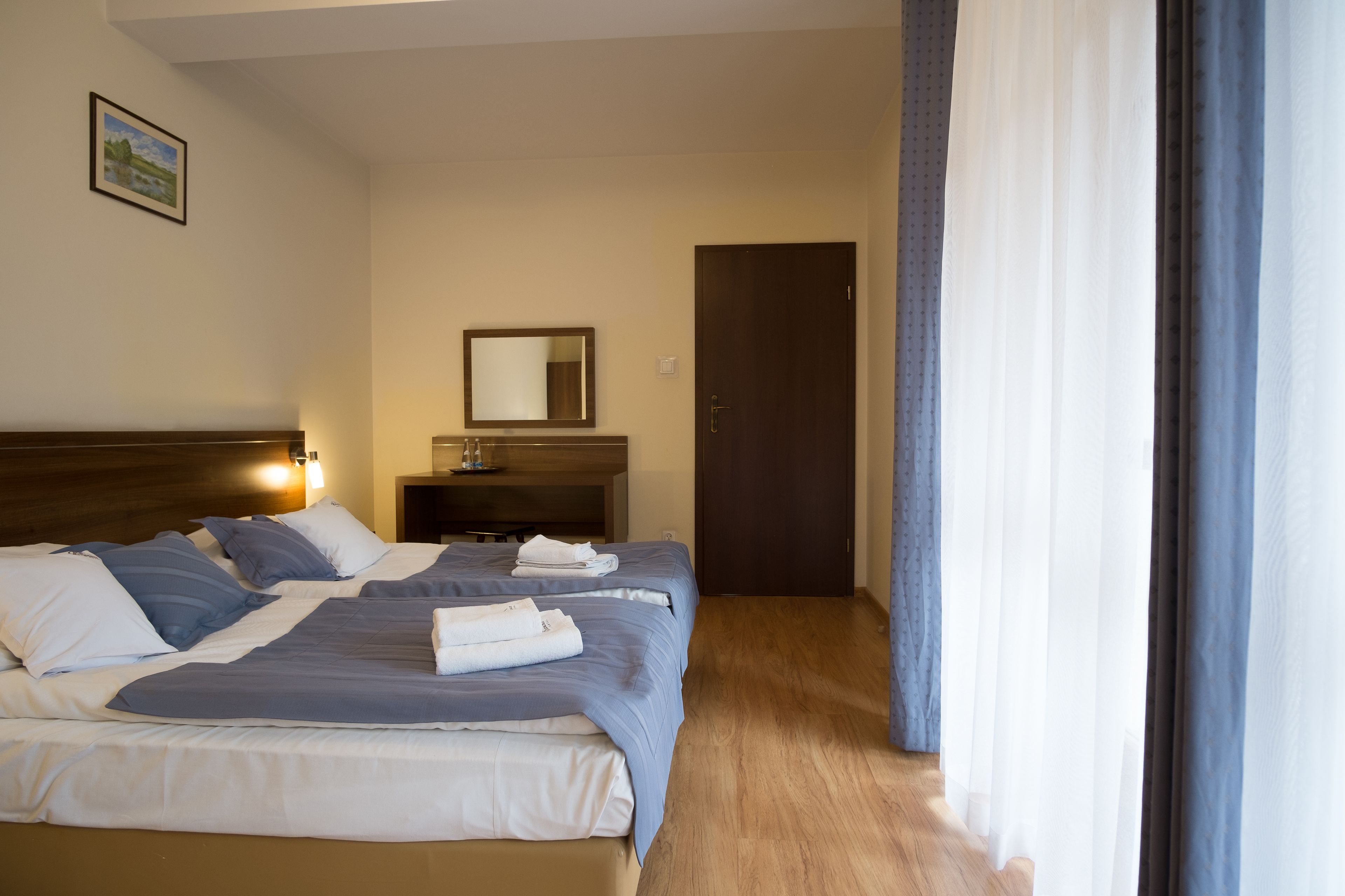 A hotel room with a bed, a bedside table, a mirror, and a door.