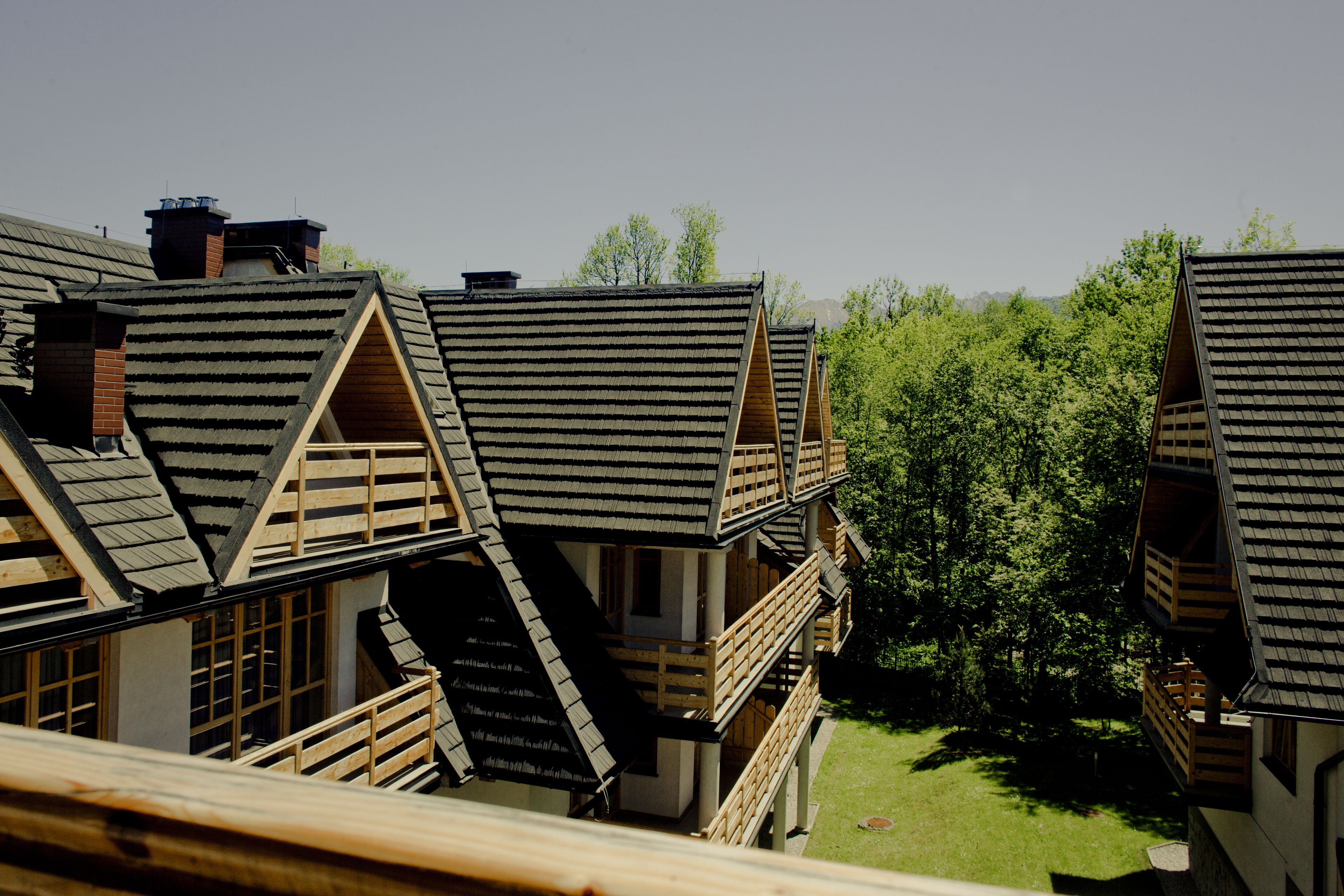 Une rangée de cabanes en bois, dotées de toits à forte pente, de balcons en bois et d’une cour verdoyante.