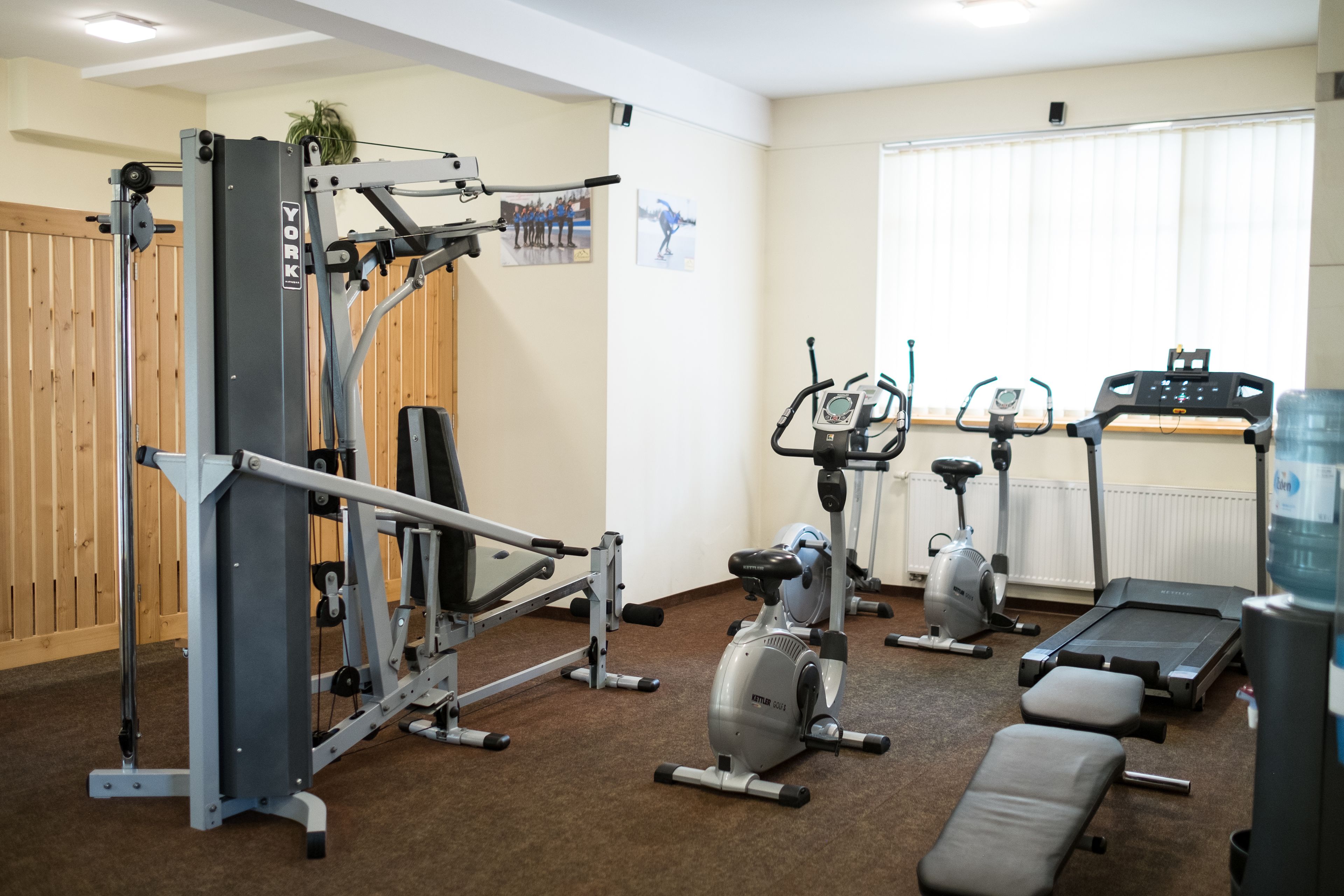 Un gimnasio con diversos equipos de ejercicio, incluyendo una cinta de correr, bicicletas estáticas y máquinas de pesas.