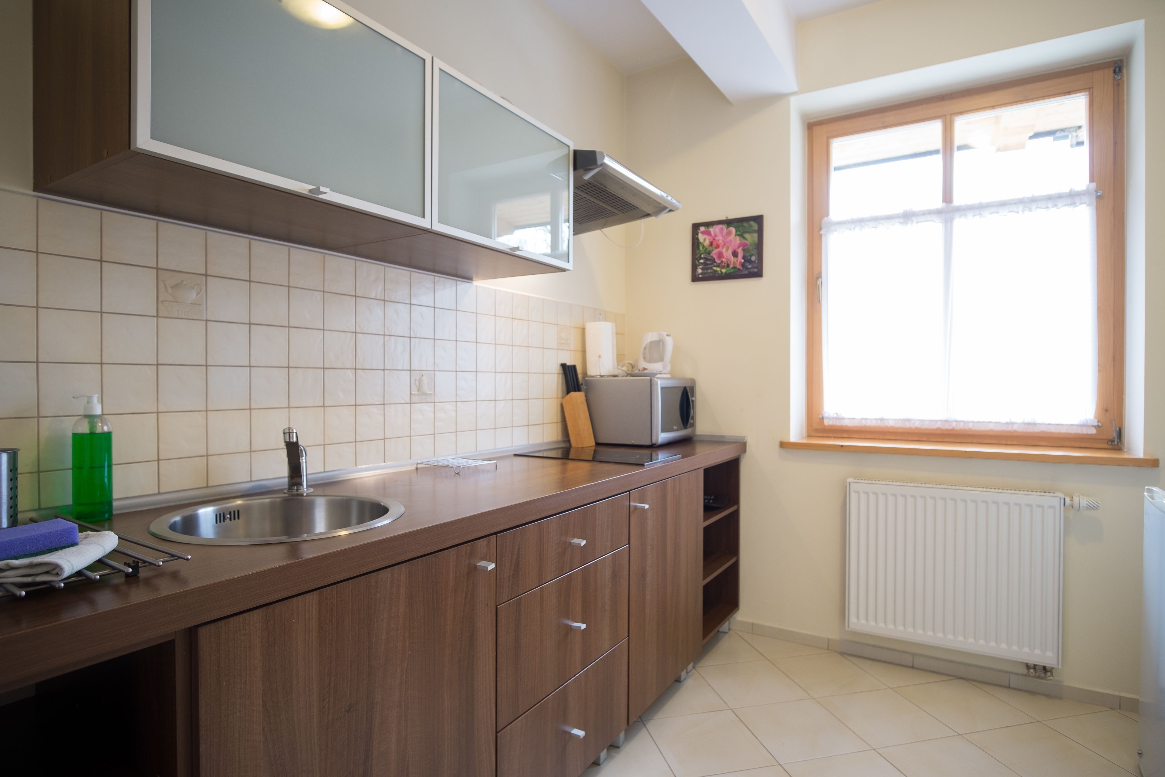 A kitchen with a stainless steel sink, wooden cabinets, a microwave, and a window with a view.