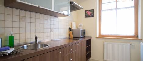 A kitchen with a stainless steel sink, wooden cabinets, a microwave, and a window with a view.