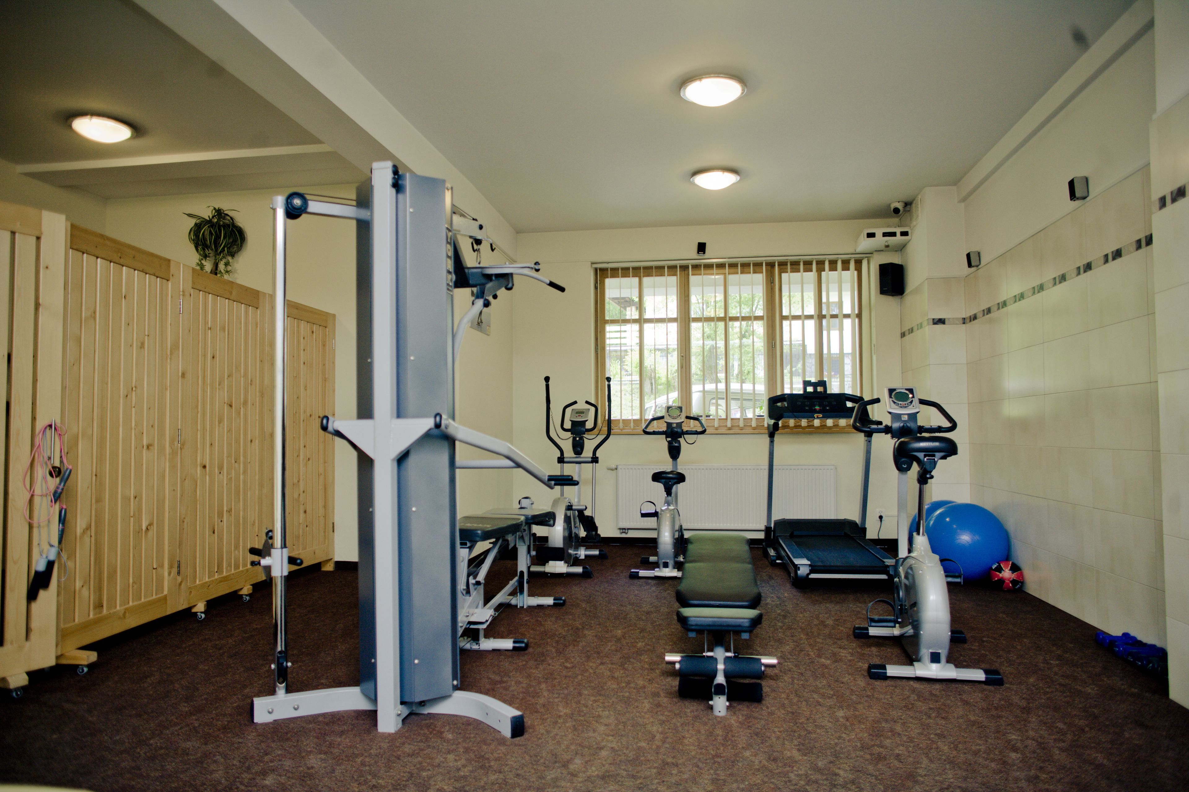A gym with various exercise equipment, a wooden partition, and a window with blinds.