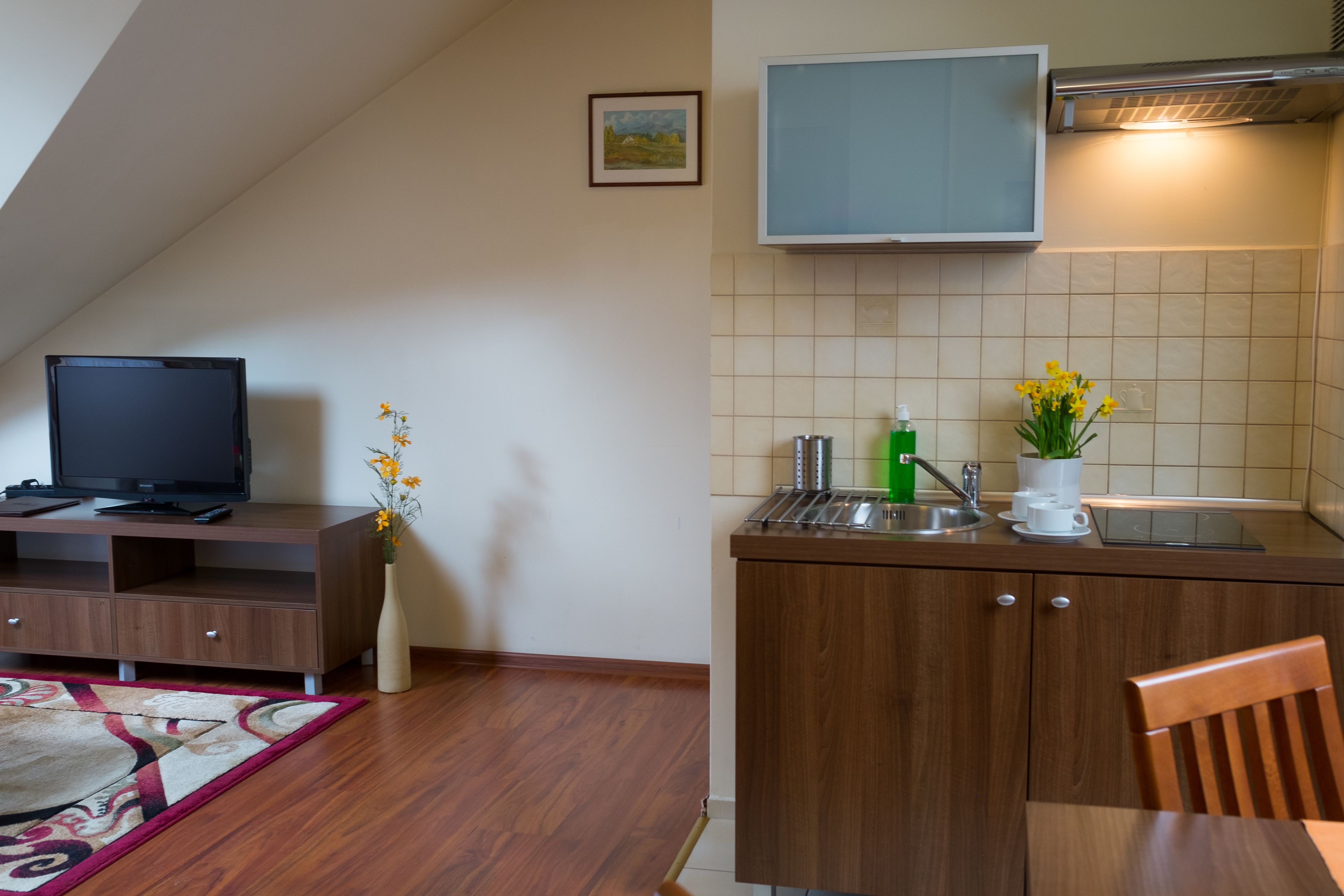 Una cocina compacta con TV integrada, un pequeño comedor con una silla y un jarrón decorativo con flores.