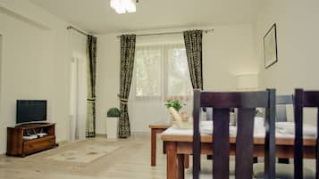 A living room with a wooden dining table, a television on a wooden stand, and a potted plant.
