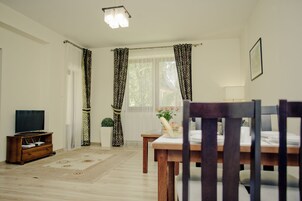 A living room with a wooden dining table, a television on a wooden stand, and a potted plant.