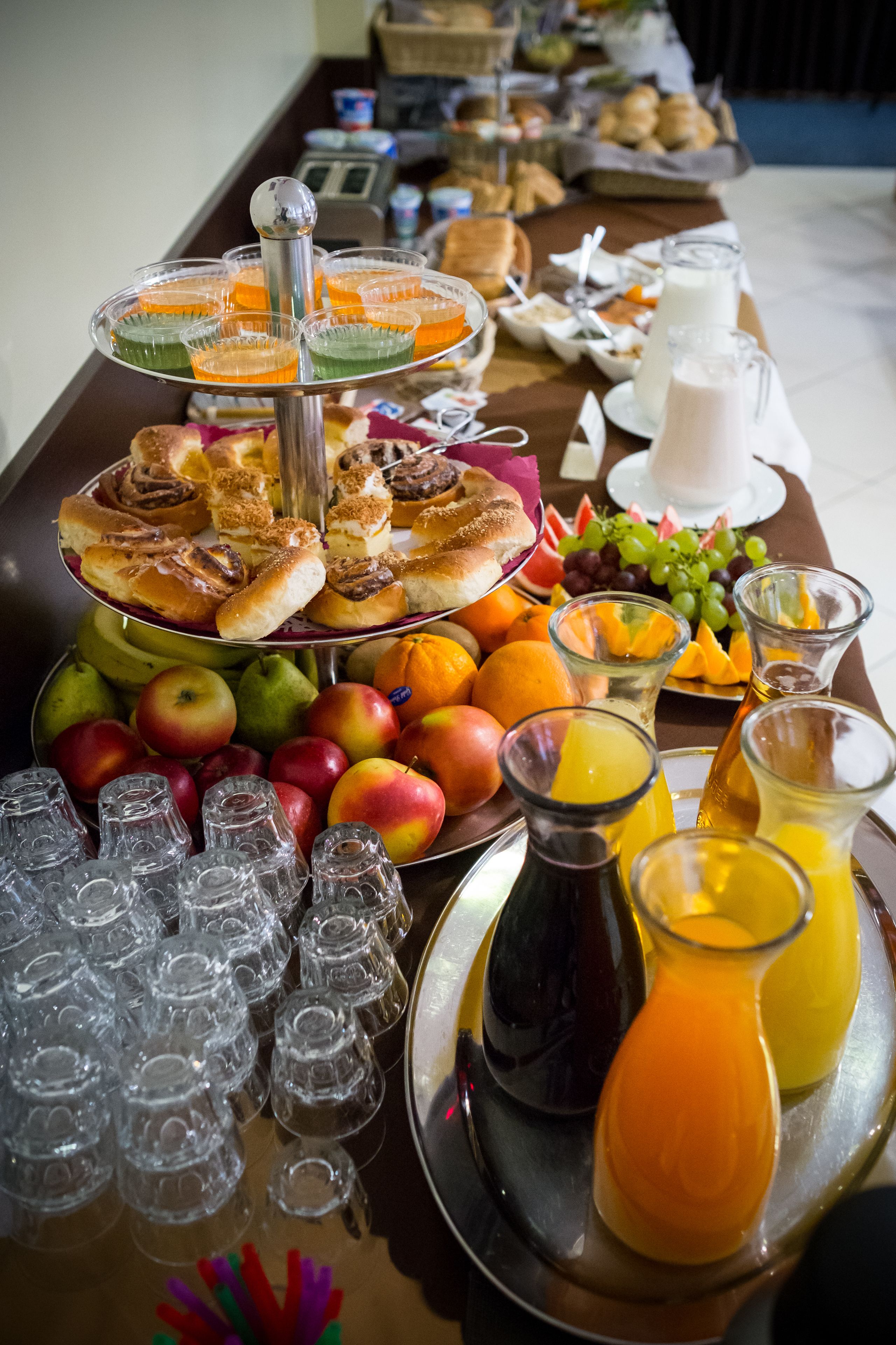 A buffet table with various food items, including fruits, pastries, and beverages.