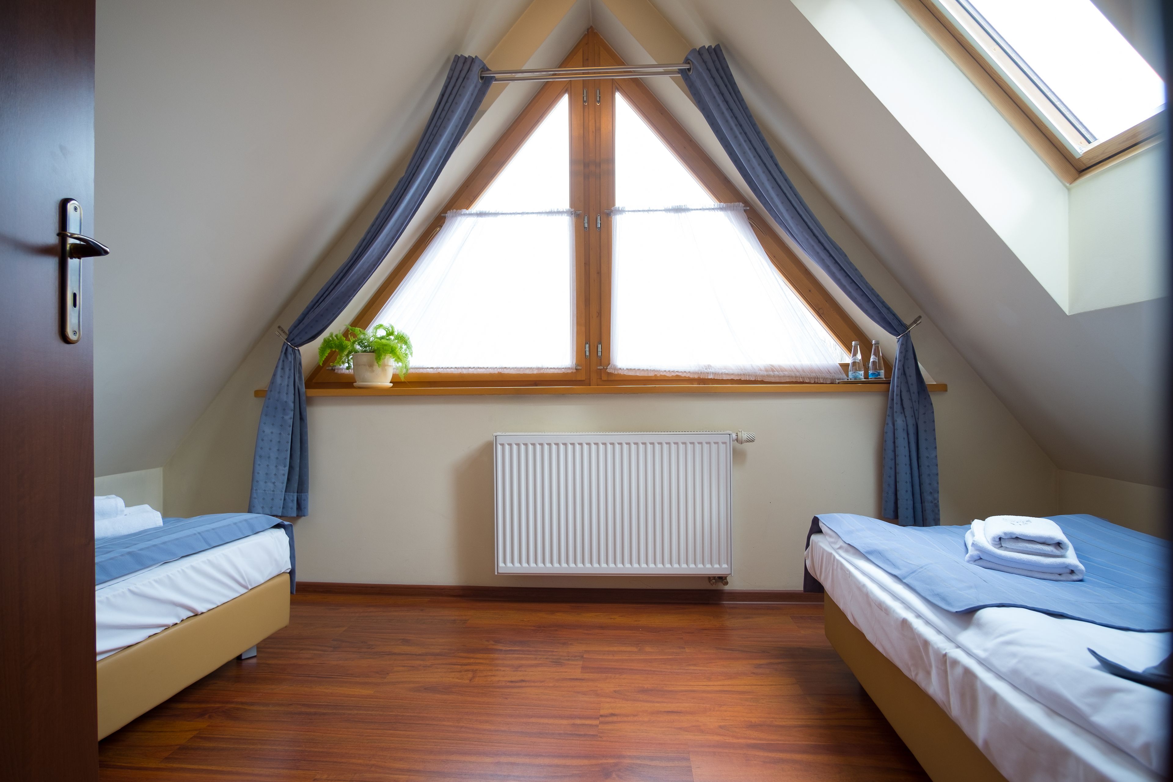 Un dormitorio con dos camas, un tragaluz, un radiador y una ventana con cortinas.