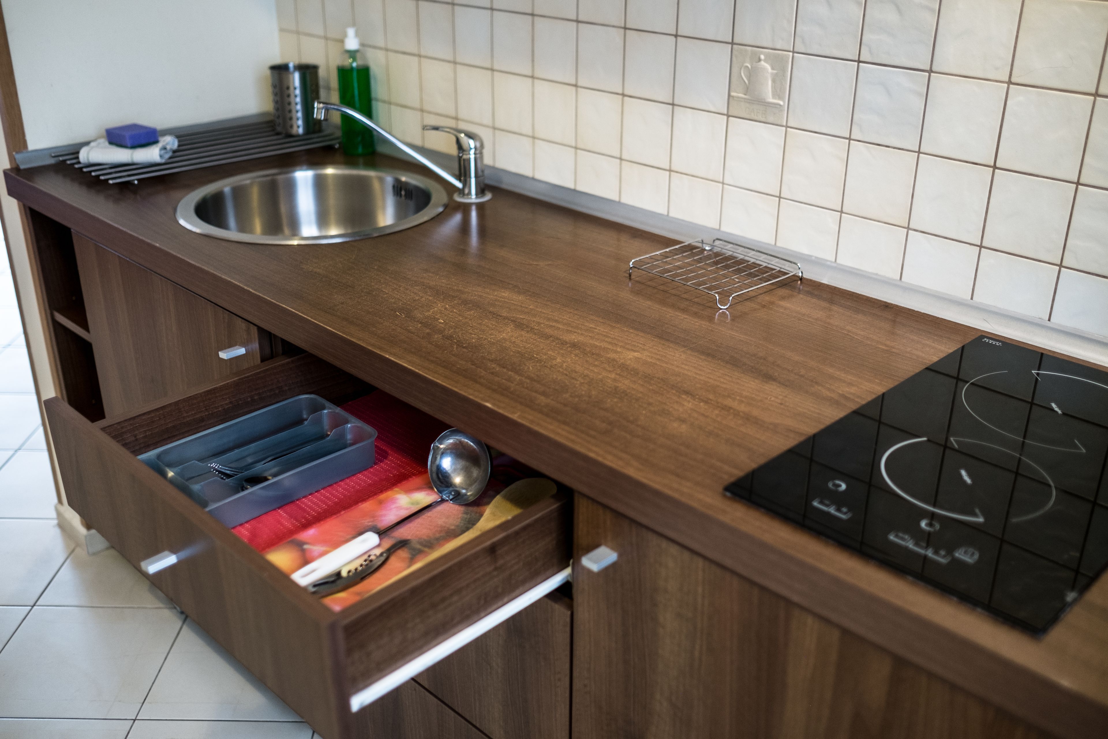 A kitchen with a stainless steel sink, wooden countertop, and a drawer with utensils.