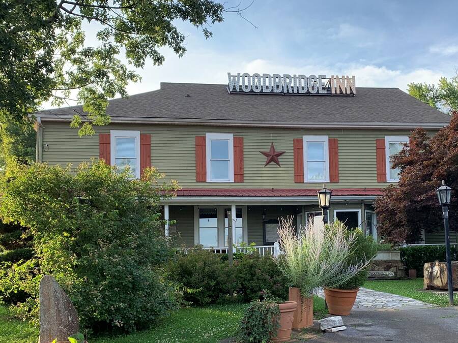 A two-story building with a sign reading "WOODERIDGE CANN". It features a porch with columns, a star decoration above the entrance, and a garden with potted plants and a stone pathway.