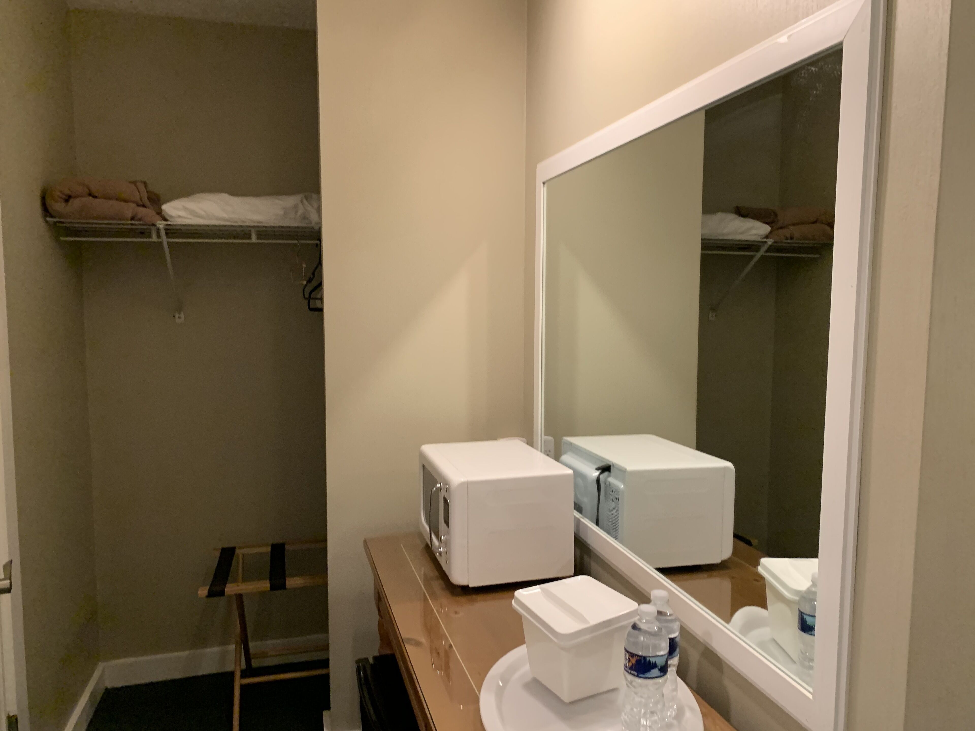A bathroom with a mirror, a microwave, a small refrigerator, a towel rack, and a shelf with towels.