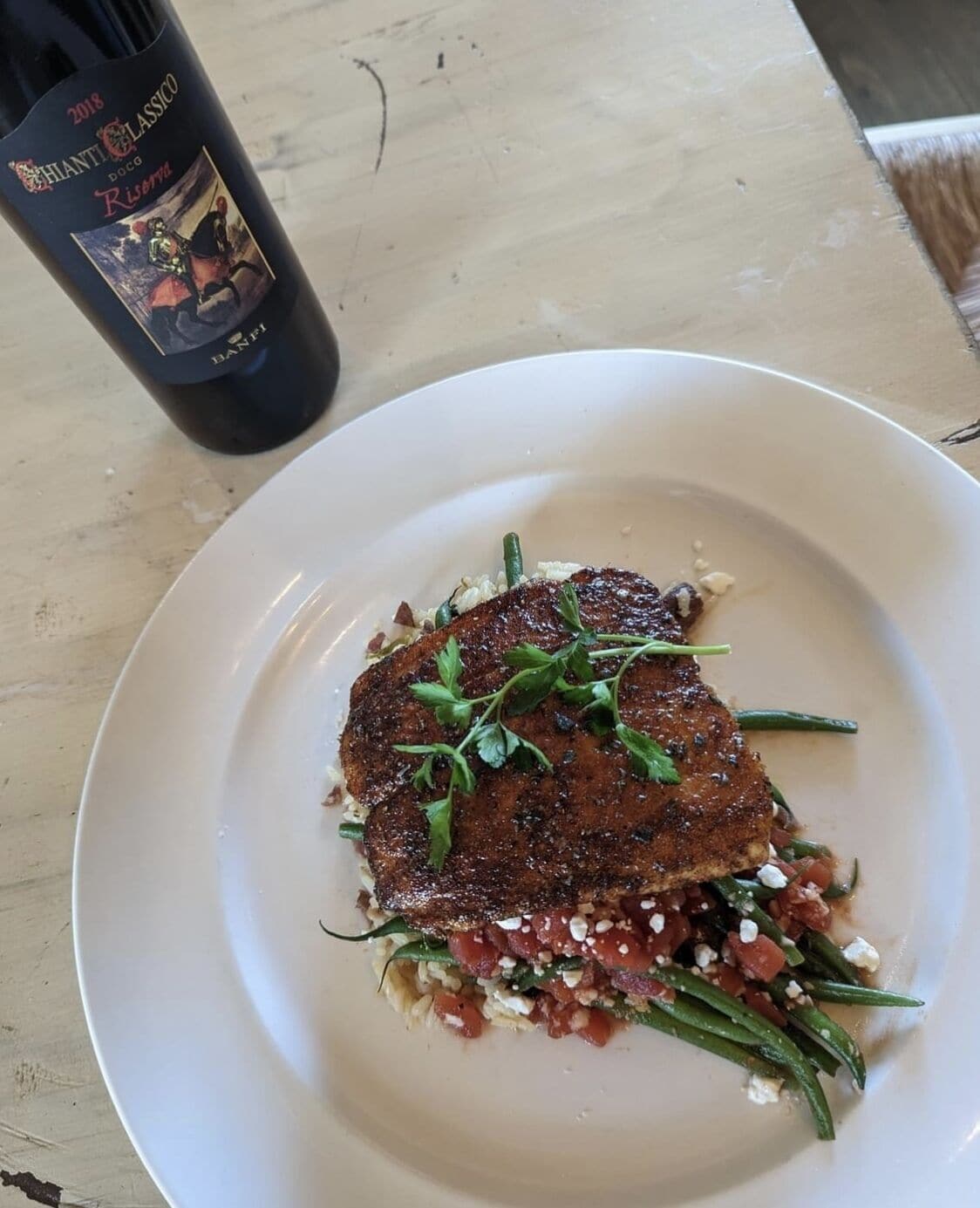 Een bord met steak en groenten, en een fles wijn op een tafel.