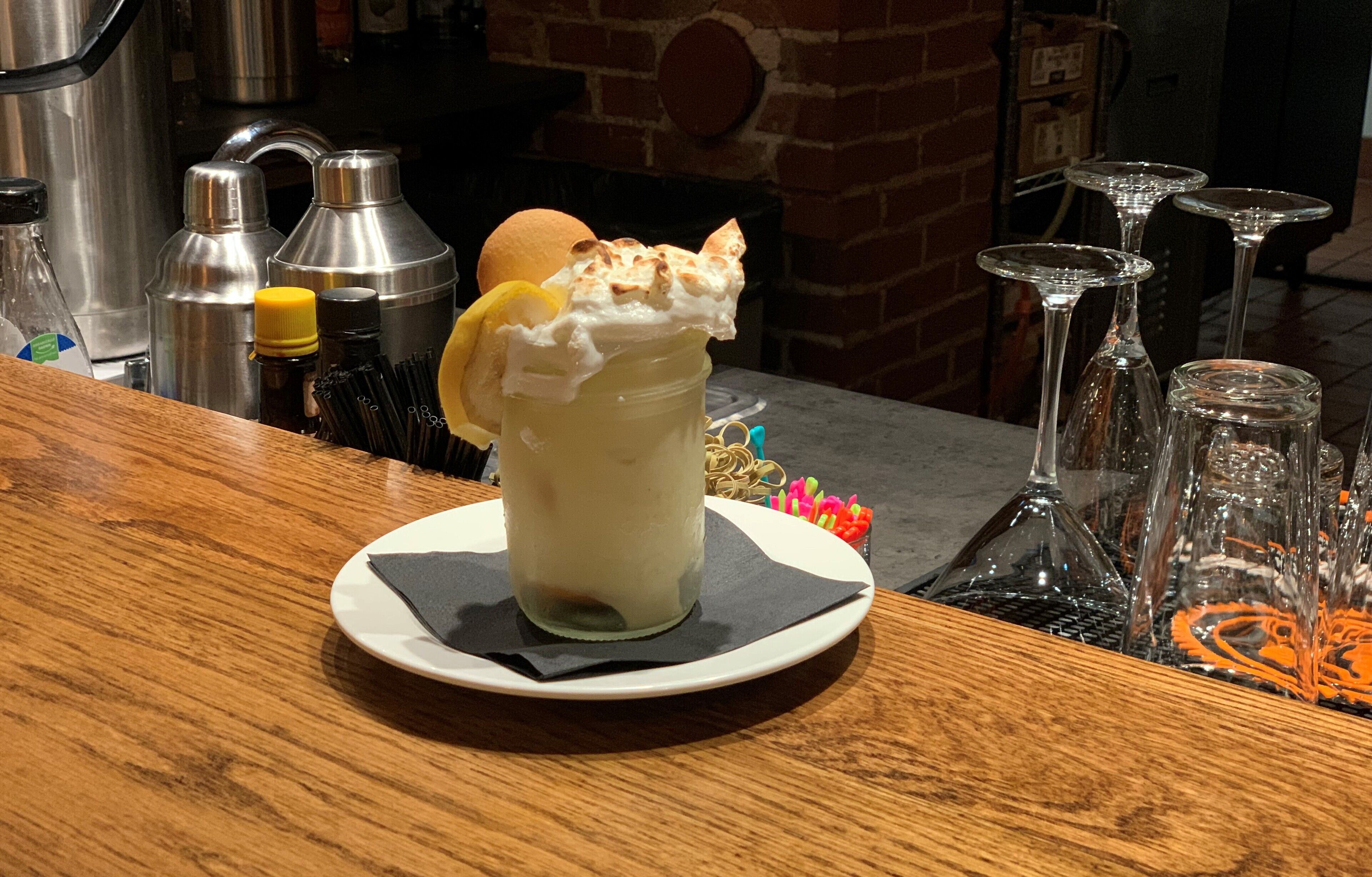 A dessert in a glass jar with whipped cream and a lemon slice on a wooden table.