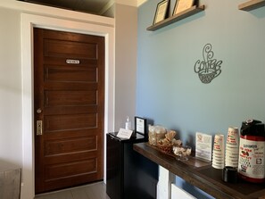 A wooden door labeled "PRIVATE" with a small black trash bin beside it. A wall-mounted sign reads "WIFI" and "The Coffee Roaster."