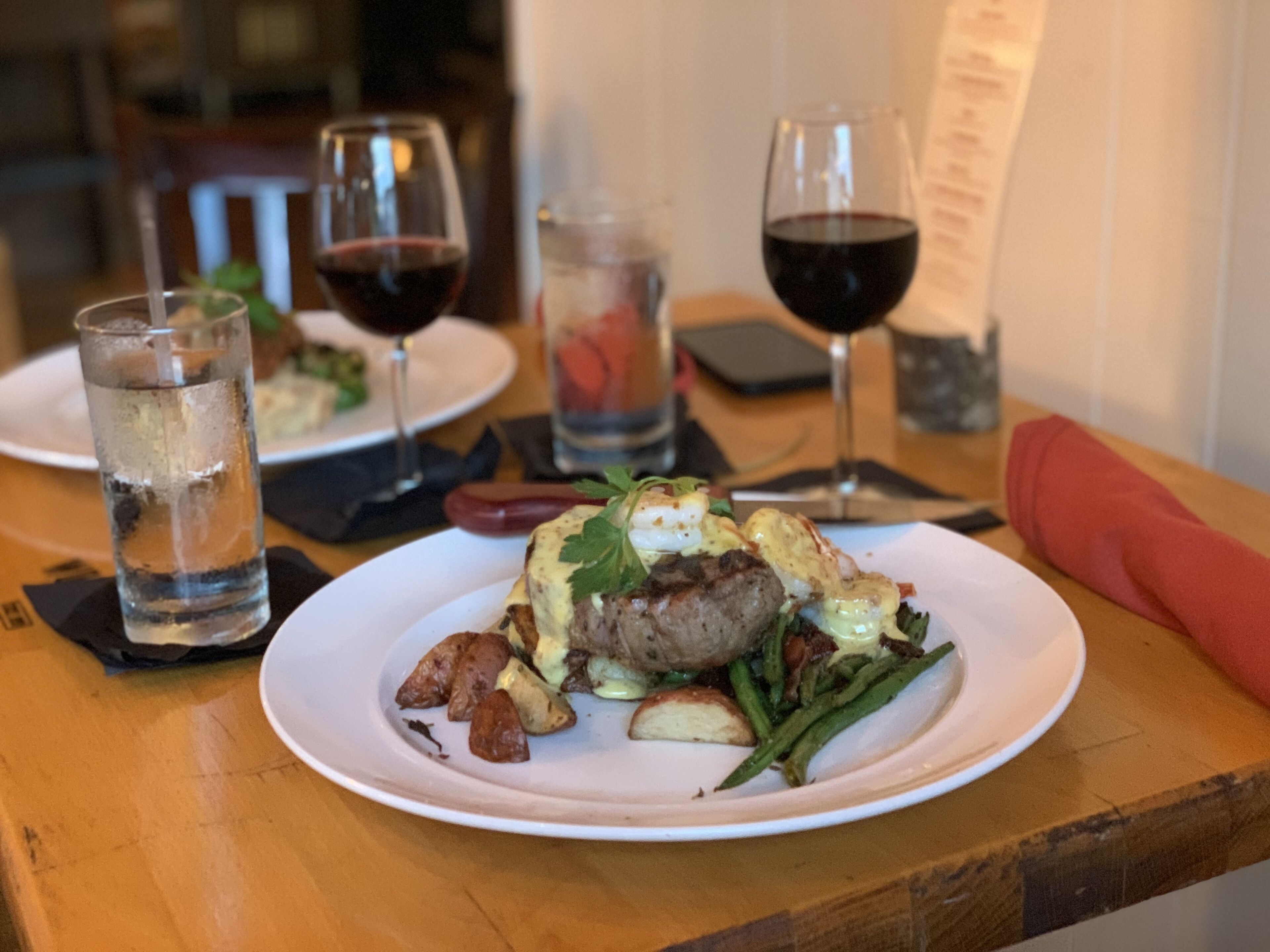 A dining table with plates of food, glasses of water and wine, and a menu.