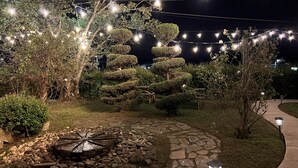 Un jardín nocturno con un sendero de piedra, arbustos bien cuidados y luces de cuerda.