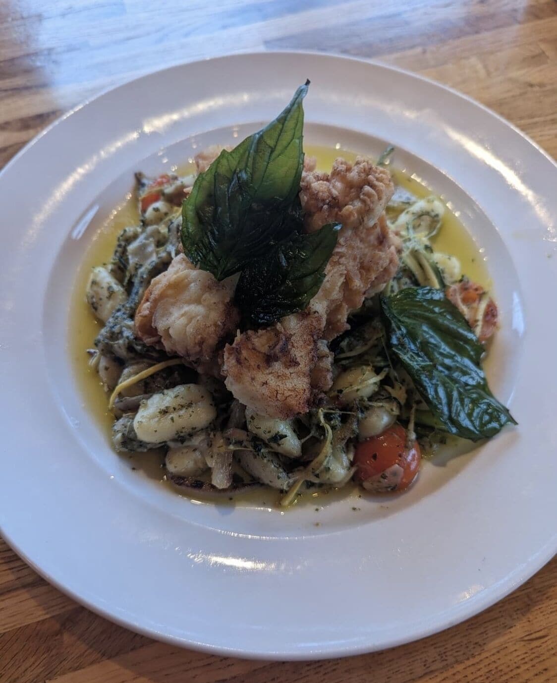 A plate of food with a piece of fish, vegetables, and a basil leaf garnish.