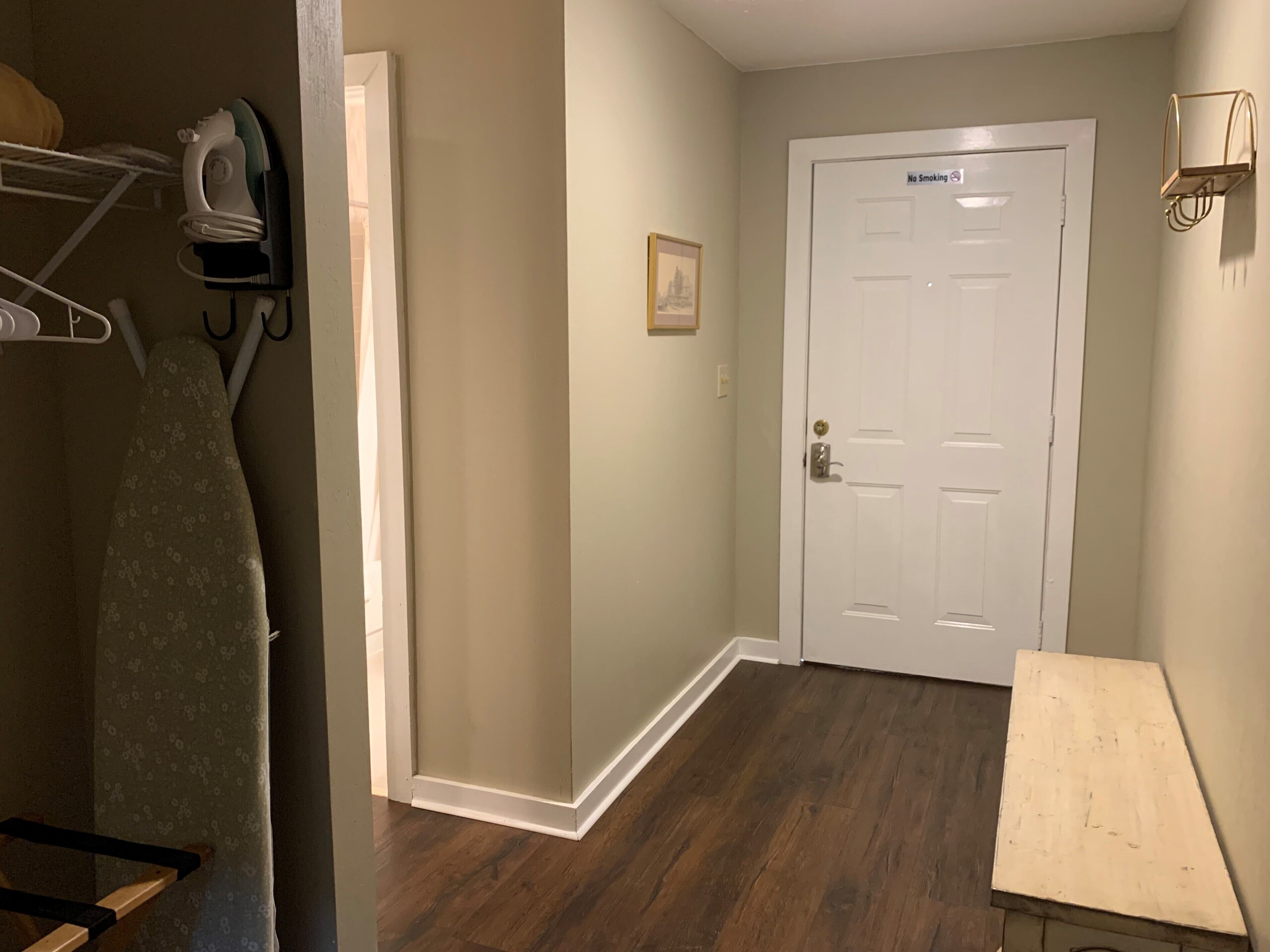 A hallway with a wooden floor, a white door with a 'No Smoking' sign, and a wall-mounted light fixture.