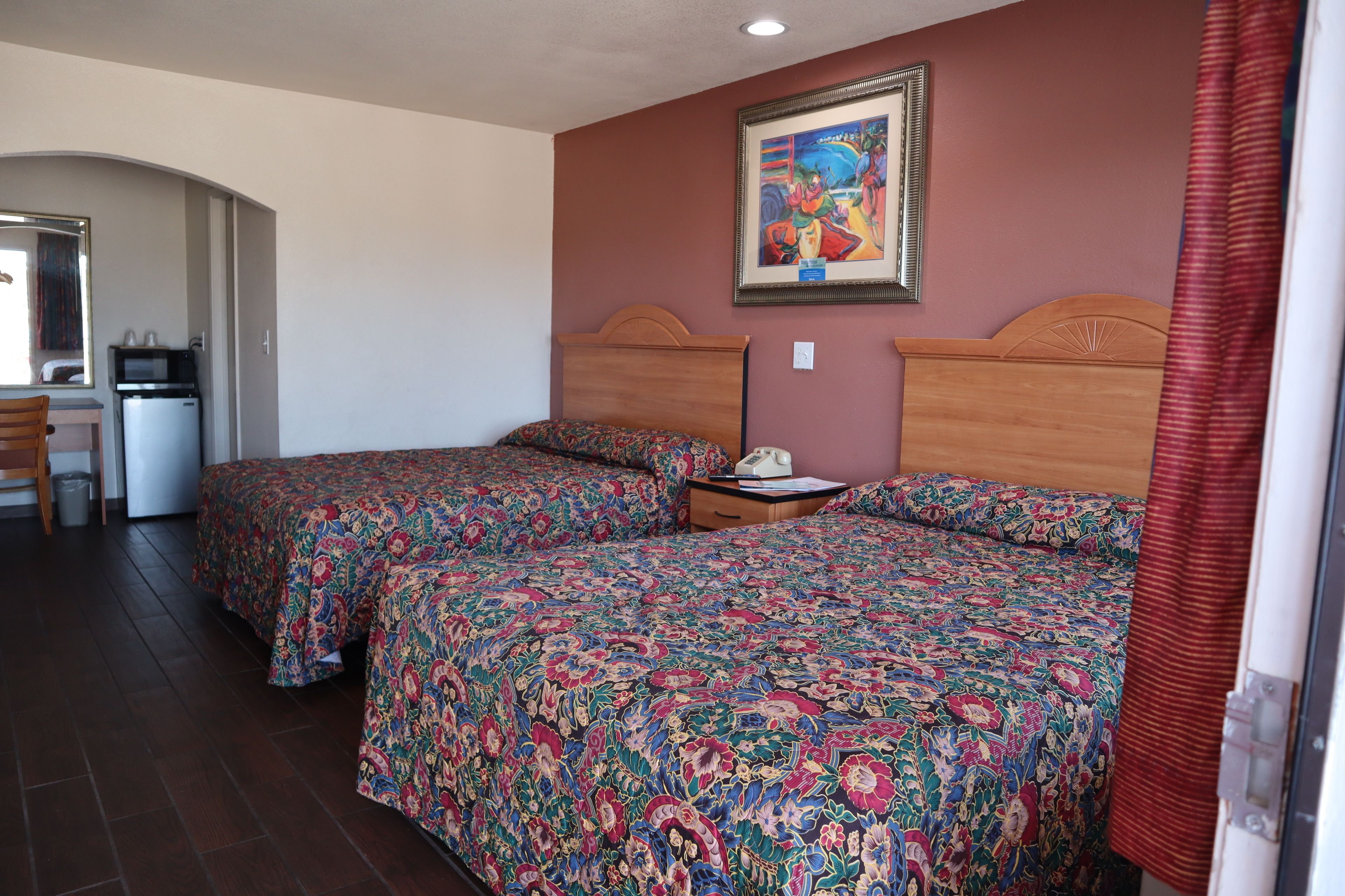 Habitación de hotel con dos camas, un escritorio pequeño, un refrigerador y un cuadro en la pared.