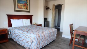 Une chambre d’hôtel avec un grand lit, une table de chevet en bois, un bureau avec une chaise, un four à micro-ondes et un espace douche.