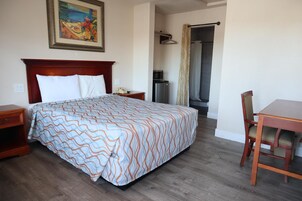 Una habitación de hotel con una cama grande, una mesita de noche de madera, un escritorio con una silla, un microondas y una zona de ducha.