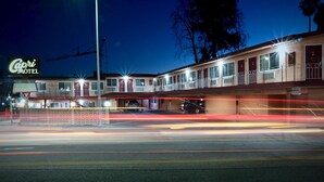 Un motel avec une enseigne indiquant « Capri Motel » et un parking où l’on peut voir des traînées de lumière laissées par les véhicules en mouvement.
