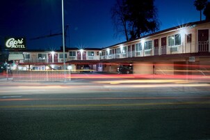 Un motel con un cartel que dice 'Capri Motel' y un estacionamiento con estelas de luz dejadas por vehículos en movimiento.