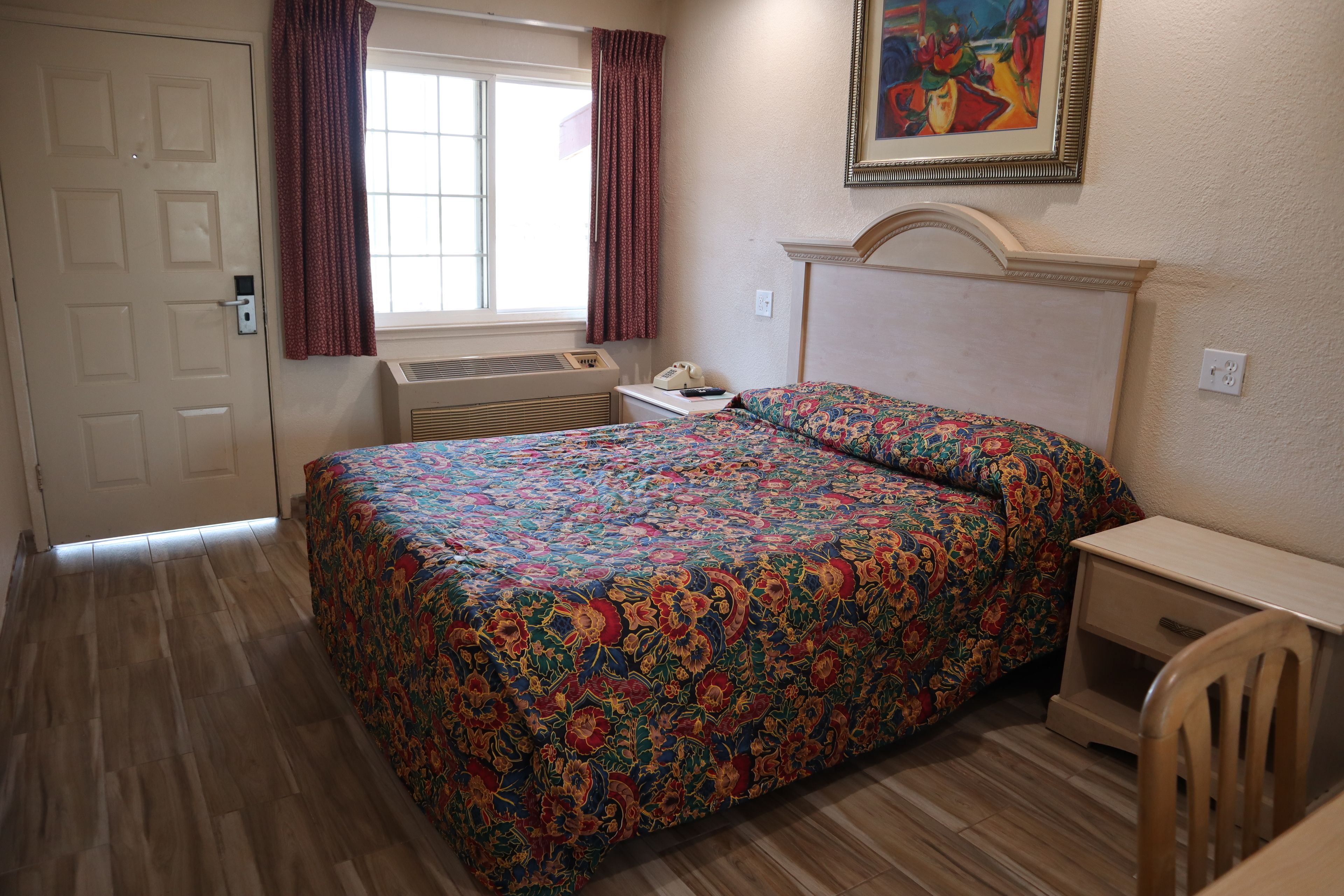 A bedroom with a bed, a desk, a chair, a window with curtains, a radiator, and a door.
