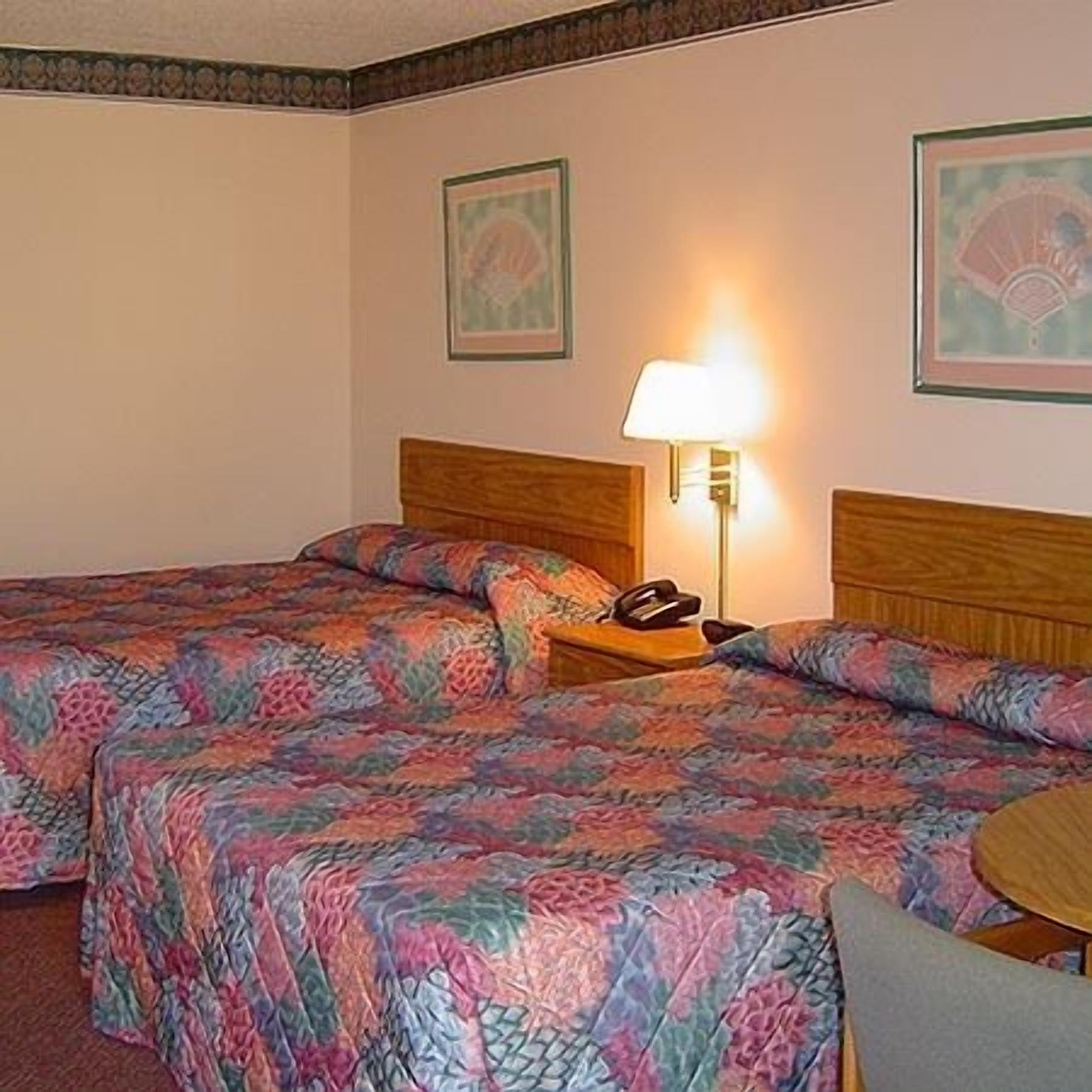 Una habitación de hotel con dos camas, una mesita de noche con lámpara y cuadros en las paredes.