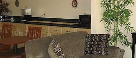 A living room with a sofa, a dining table, and a kitchen area in the background.