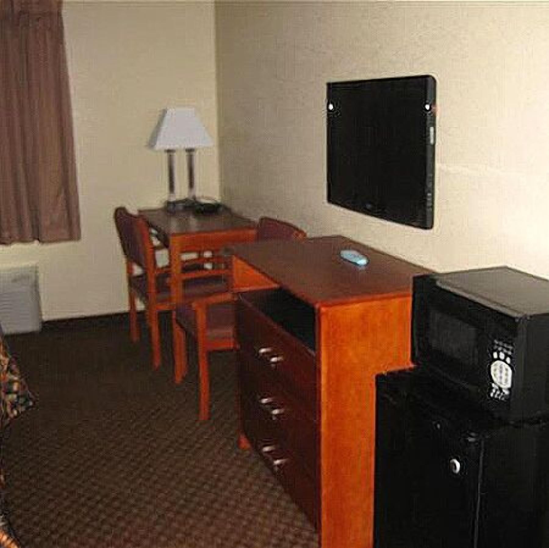 Una habitación de hotel pequeña con un escritorio de madera, una silla, una lámpara y un refrigerador negro.